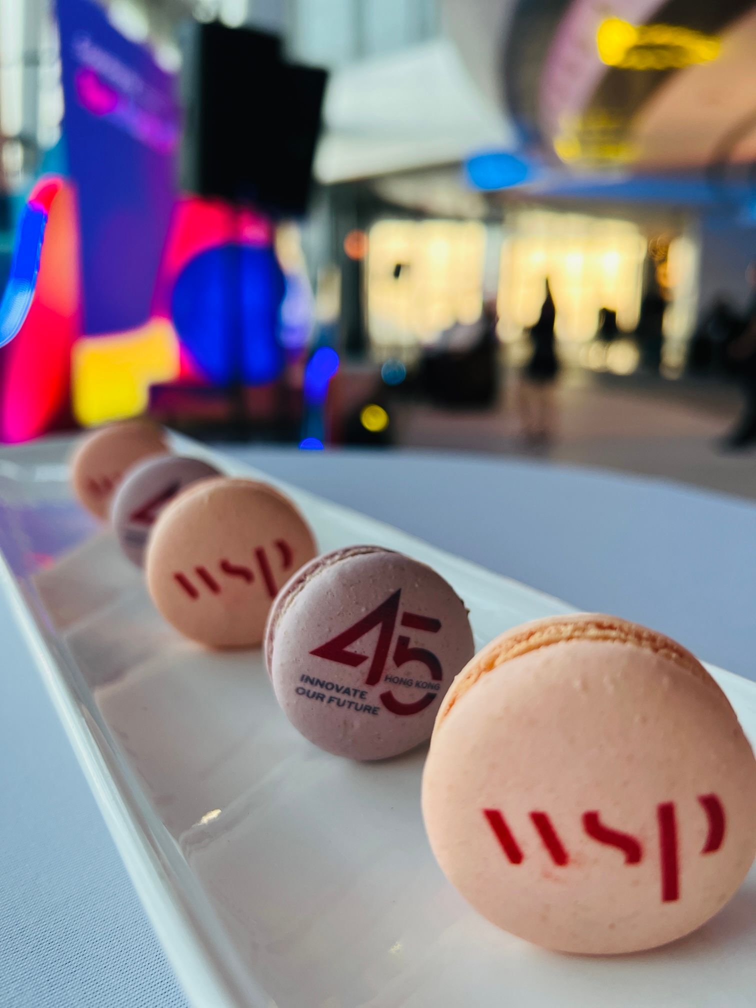 Close-up of a white platter with six custom-logo macarons in shades of pink and purple, set at an event.