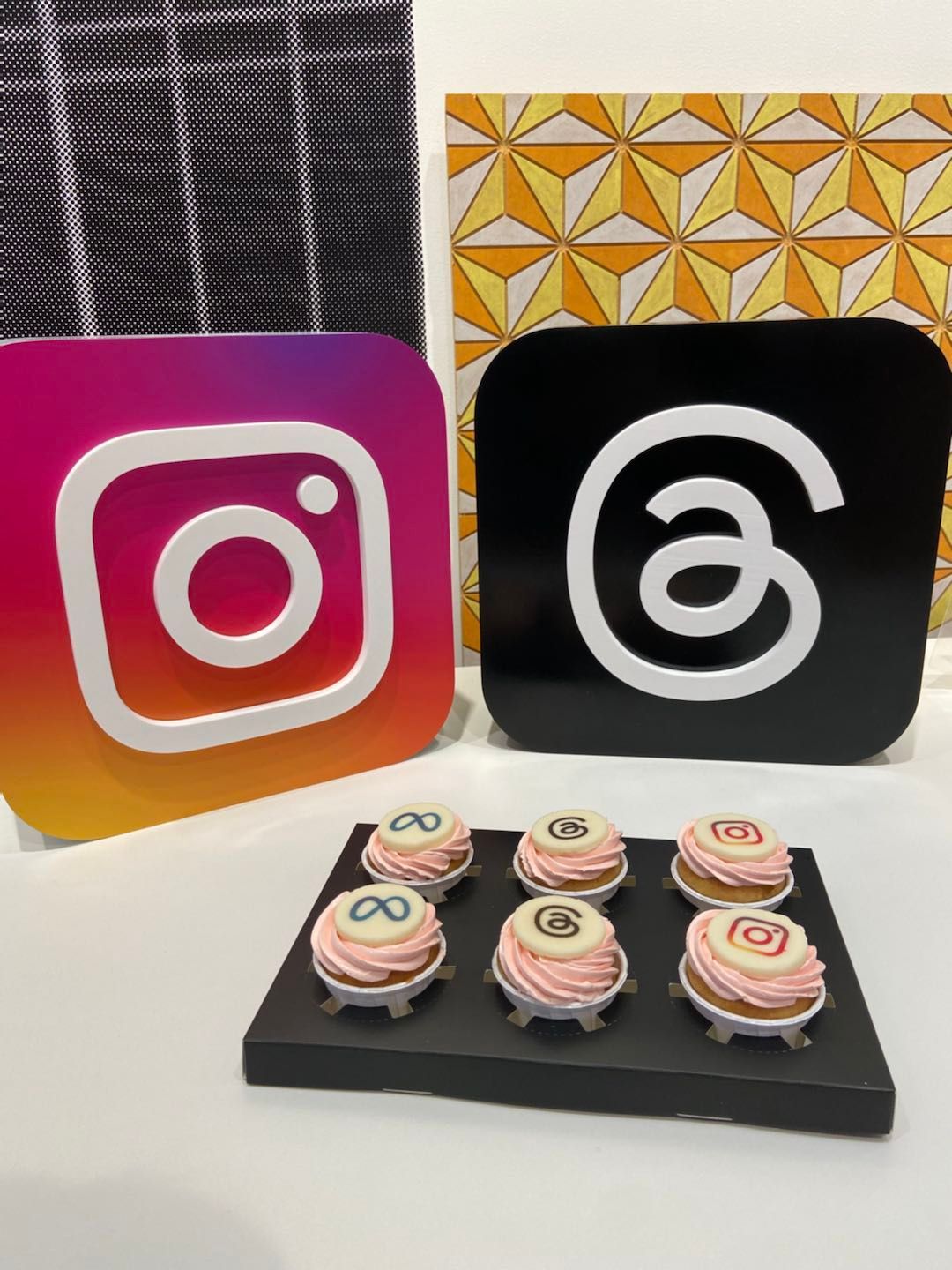Instagram and Threads logos with cupcakes, displayed near decorative art pieces.