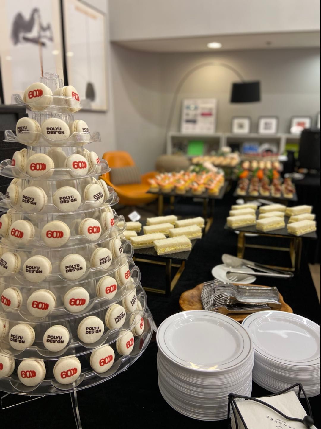 Dessert table with macaron tower, appetizers, plates, and black tablecloth.