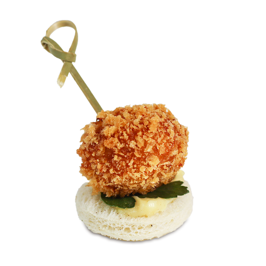 Fried food appetizer on a white bread base, skewered, with a creamy sauce and garnish.