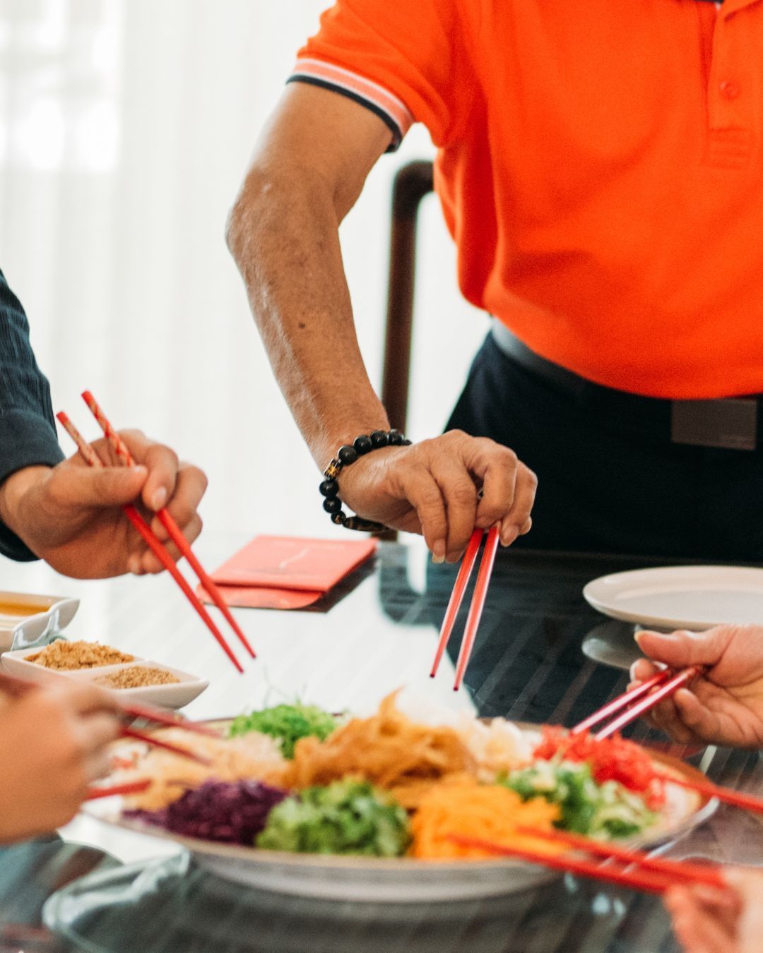 People tossing salad with chopsticks at a table, celebrating. Colorful food on a platter.