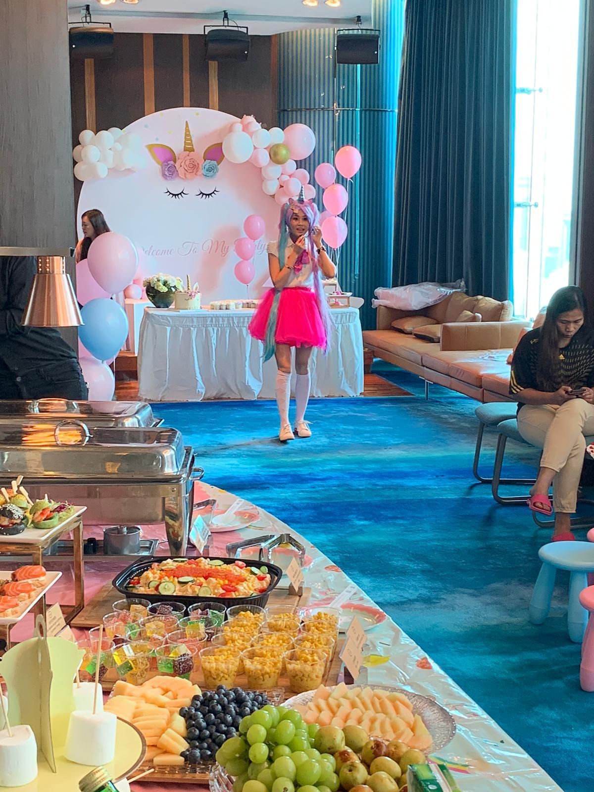 Party with unicorn decorations, buffet, and entertainer wearing pink.