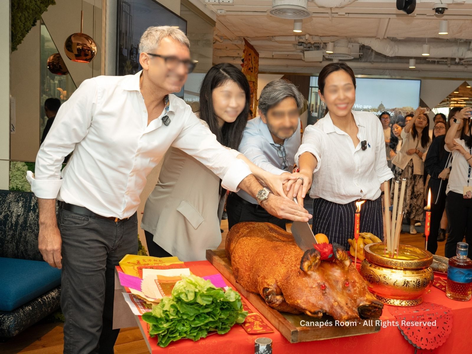 Four people cutting a roasted pig at a ceremony; table includes food, incense, and drinks.