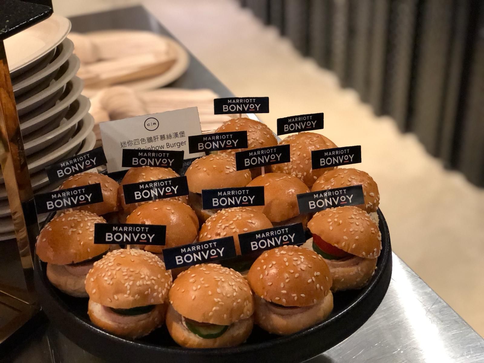 Mini burgers on a platter, each with a Marriott Bonvoy flag, ready for serving.