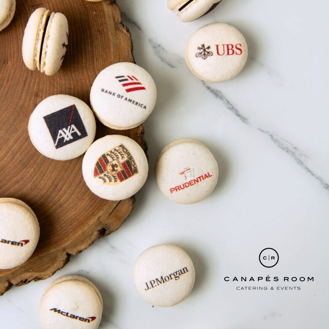 Macarons with corporate logos on a wooden board and marble surface.
