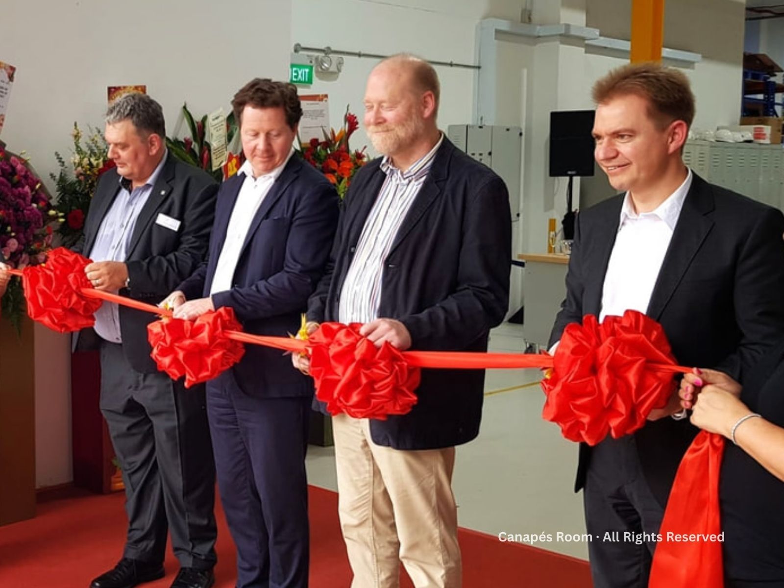 Four men cut a red ribbon with festive bows at an opening ceremony.