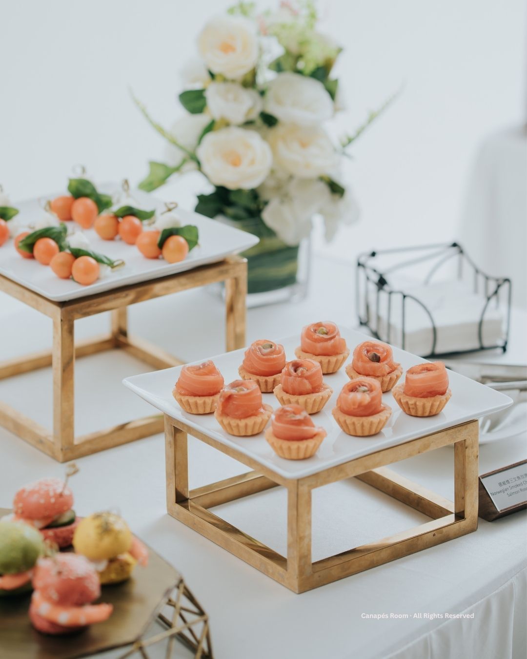 Person looking at a buffet of appetizers including sliders, and tarts under decorative lighting.