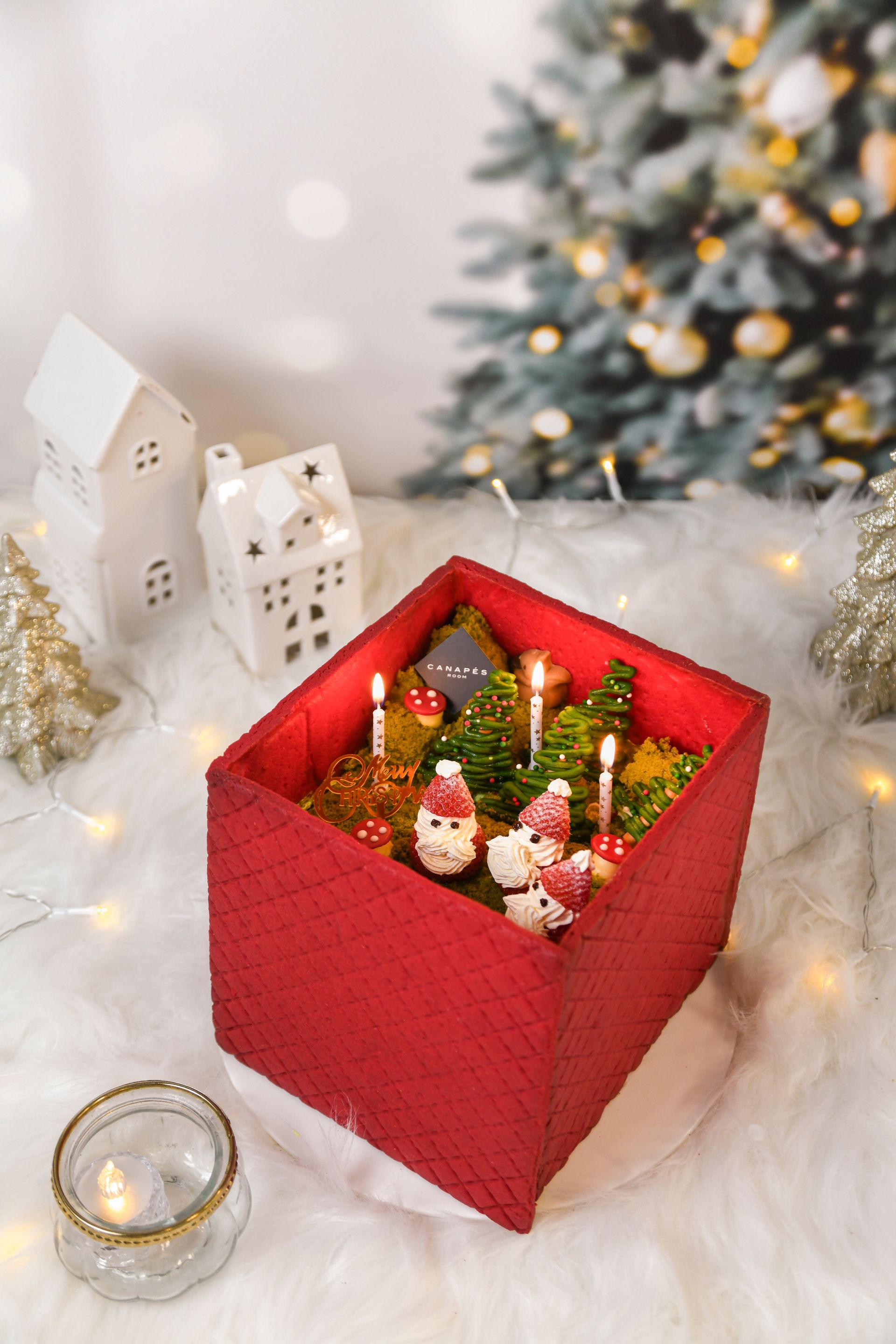 Red box Christmas diorama with miniature snowmen, candles, and trees. Festive holiday scene.