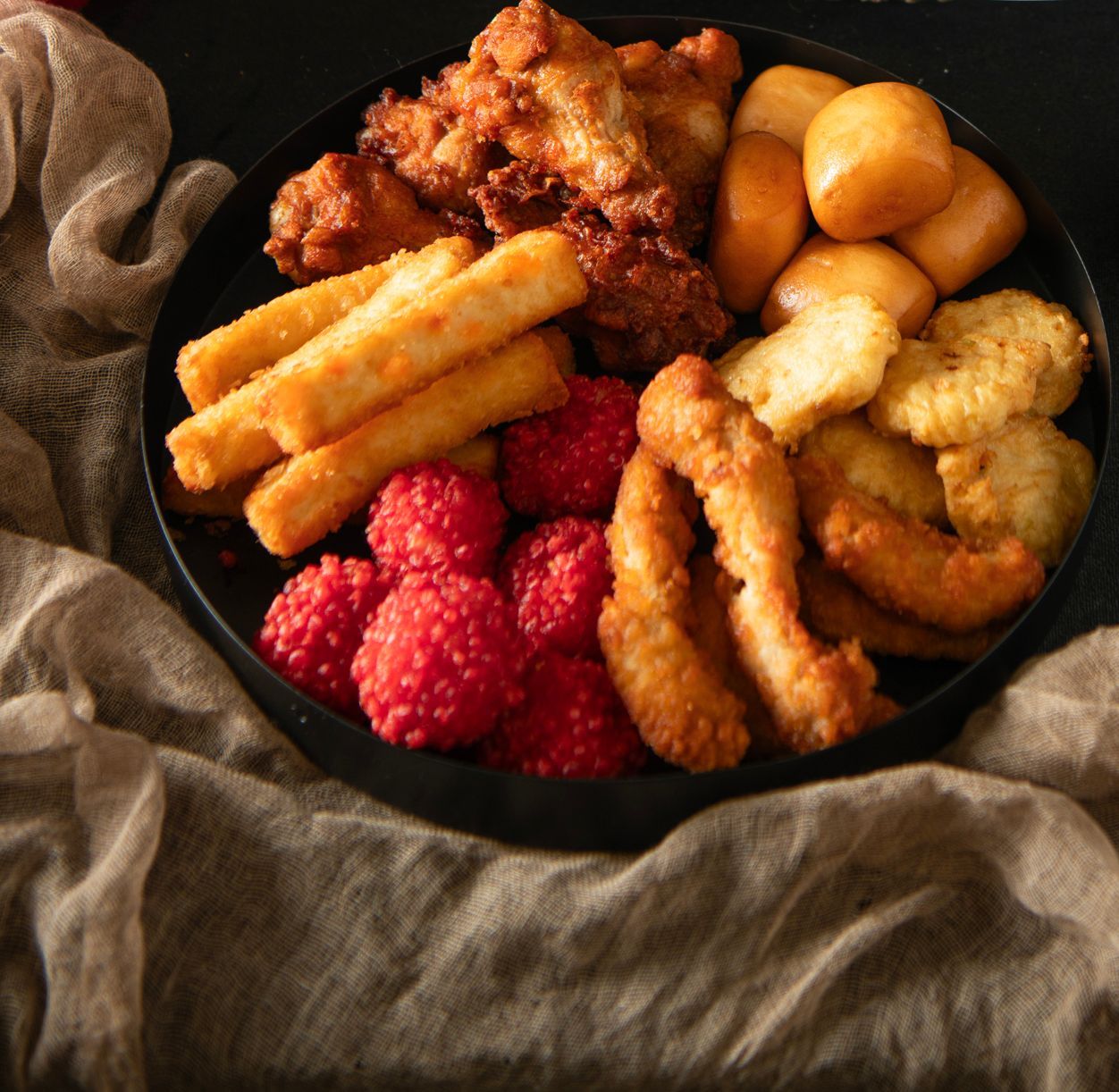 A black plate filled with fried foods: chicken, cheese sticks, dough, shrimp, and red berries.
