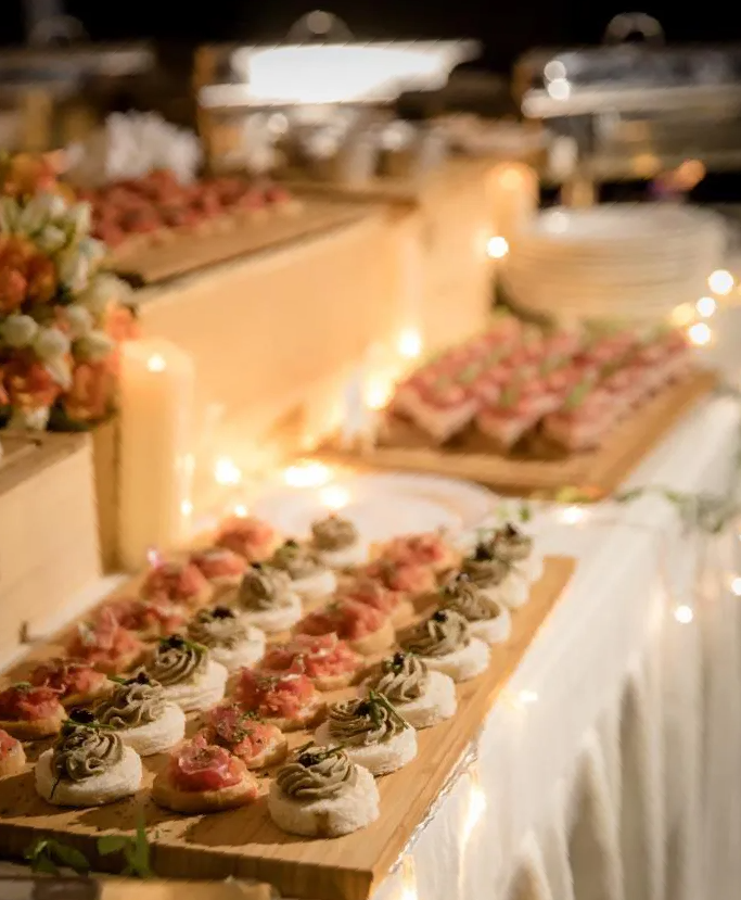 Appetizer buffet table at a catered event, featuring various bite-sized snacks on wooden serving boards.