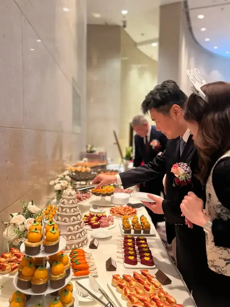 People selecting food from a buffet table at a formal event, featuring various desserts and pastries.