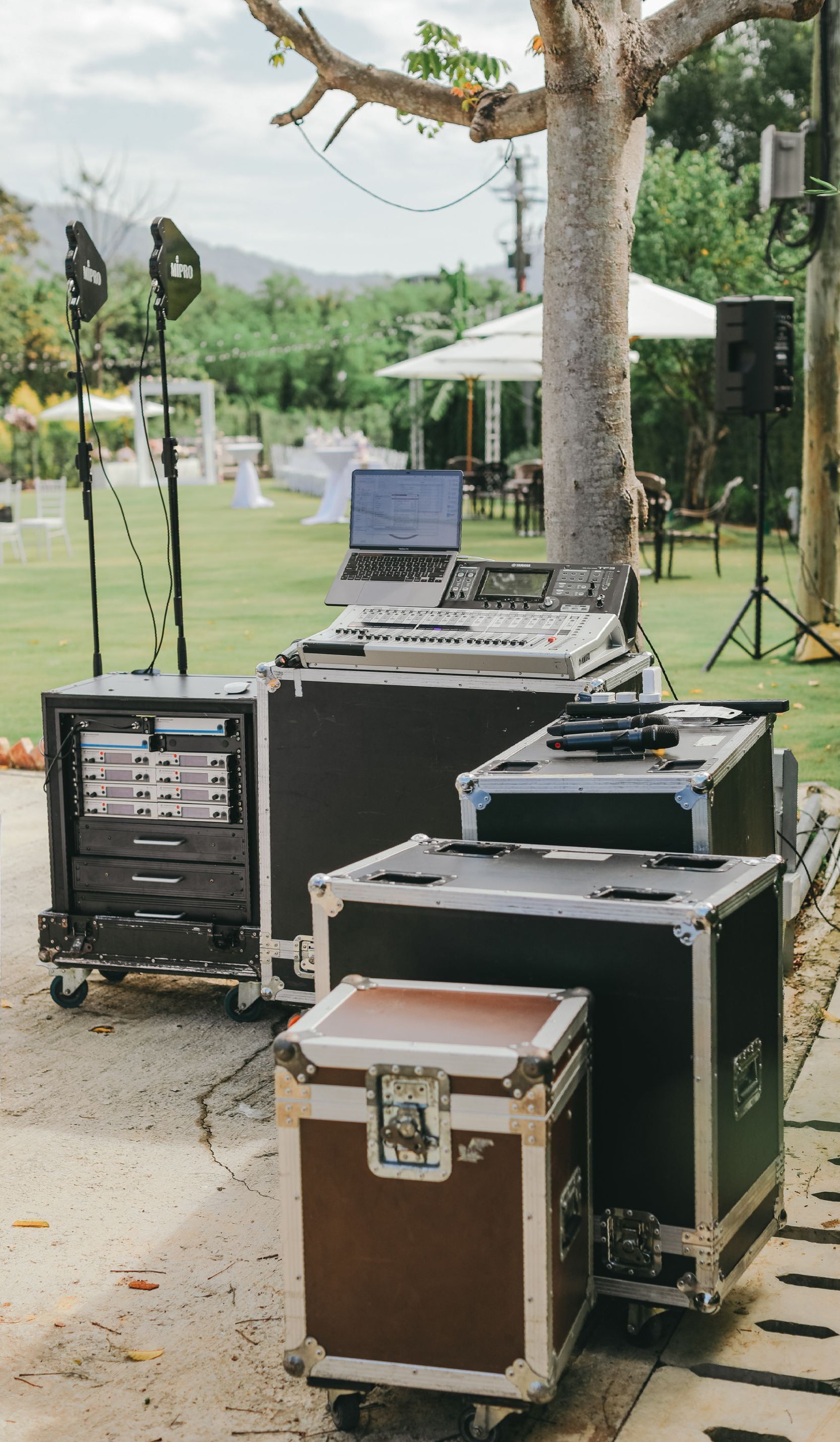DJ equipment set up outdoors on a paved area, with green lawn and trees in the background.