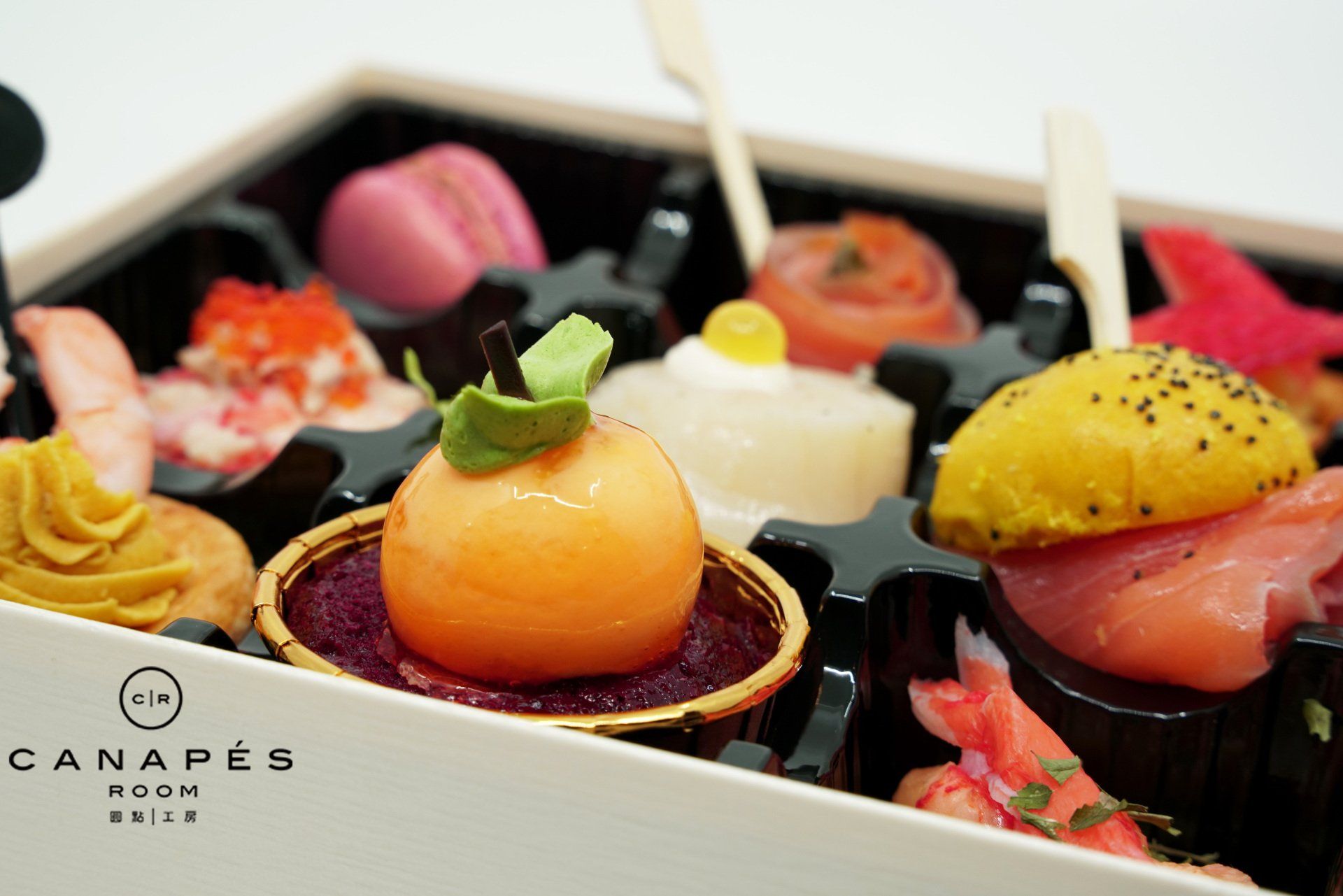 Close-up of a tray of colorful canapés, including macarons, salmon, and melon balls.