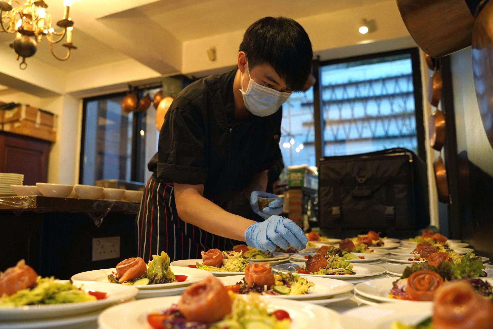 Chef in face mask and gloves plating dishes in a restaurant.