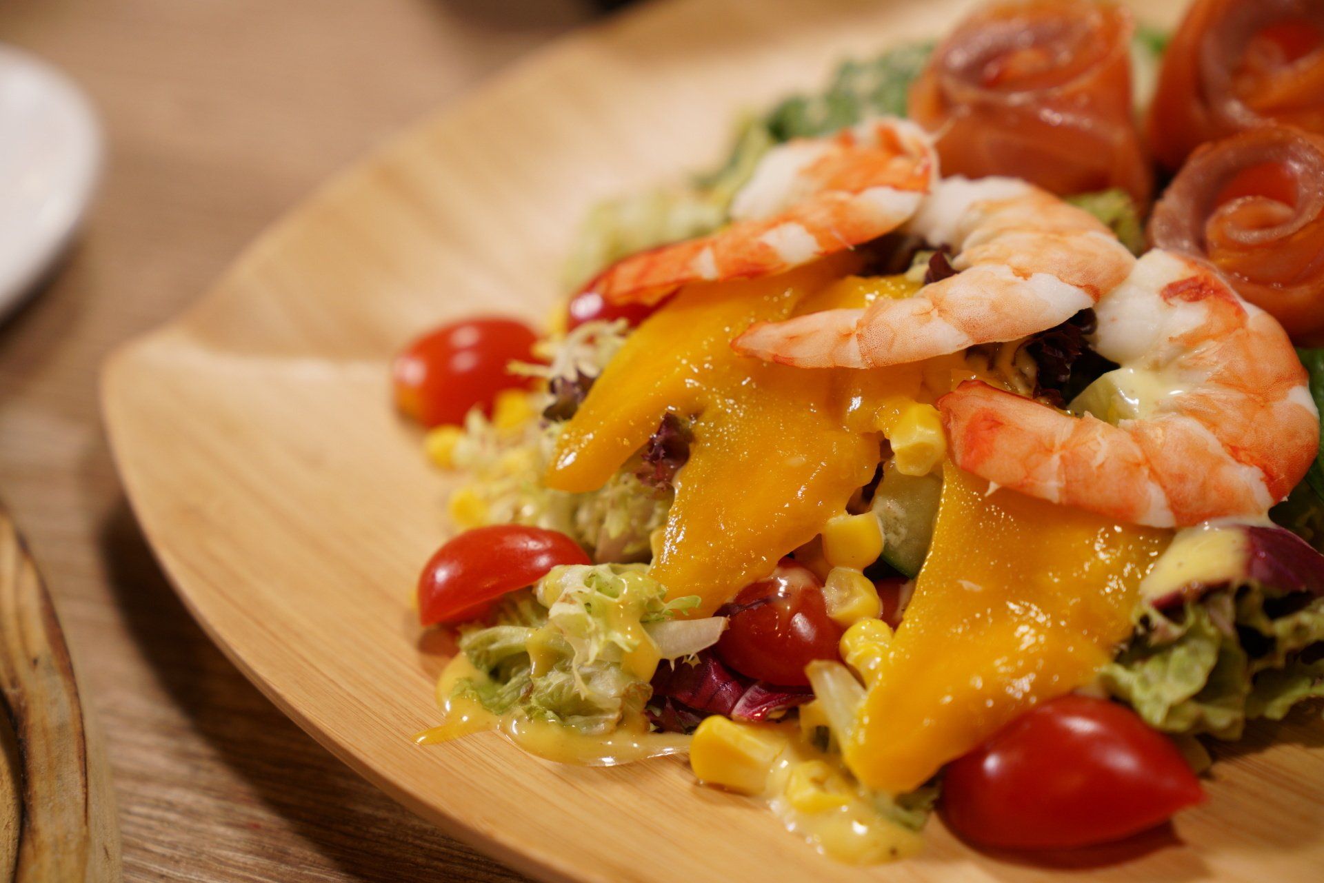 Shrimp and salmon salad with mango slices, cherry tomatoes, and corn on a wooden plate.