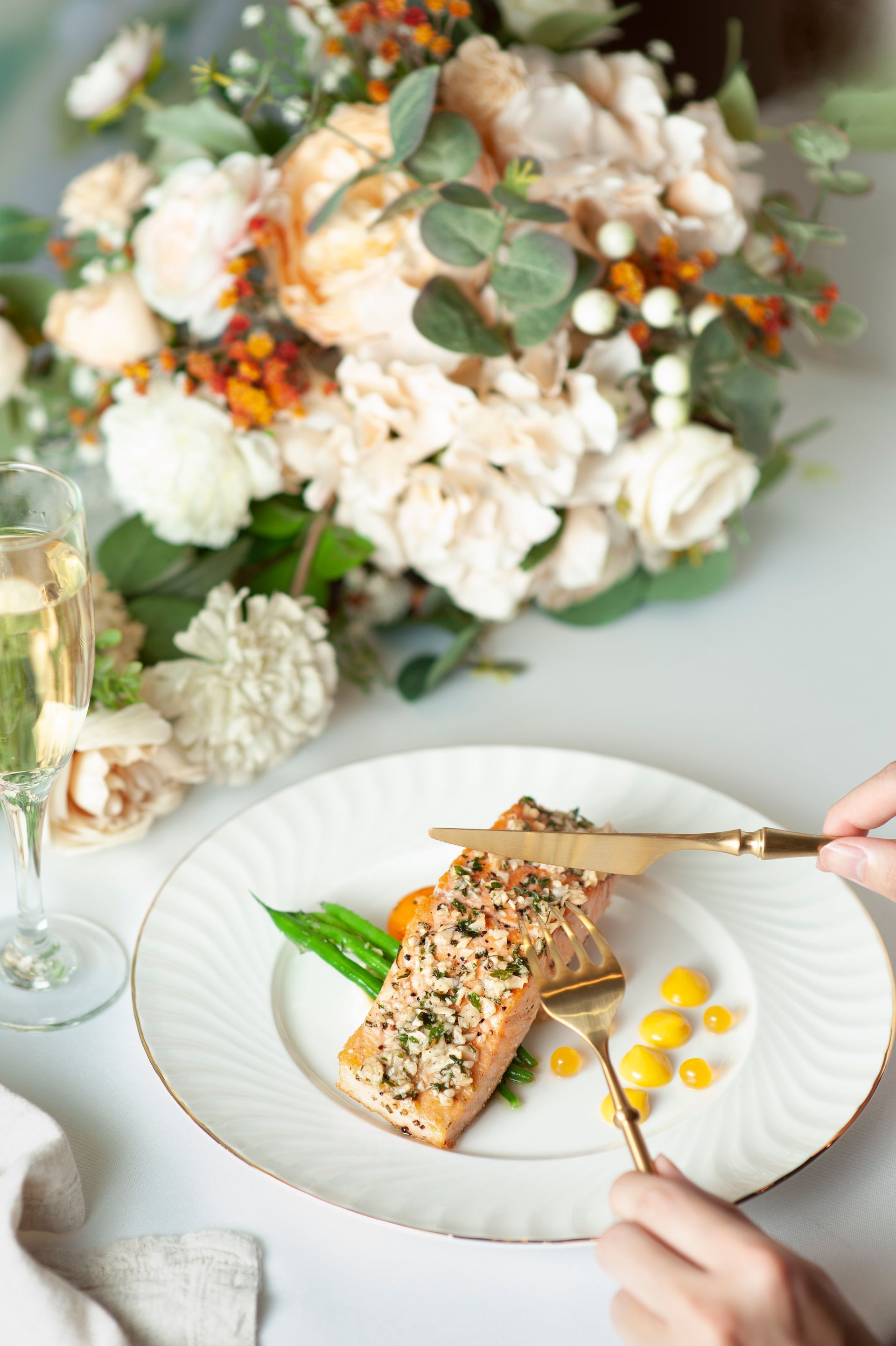 一盤鮭魚配上小菜、金色餐具和鮮花，擺在桌上。