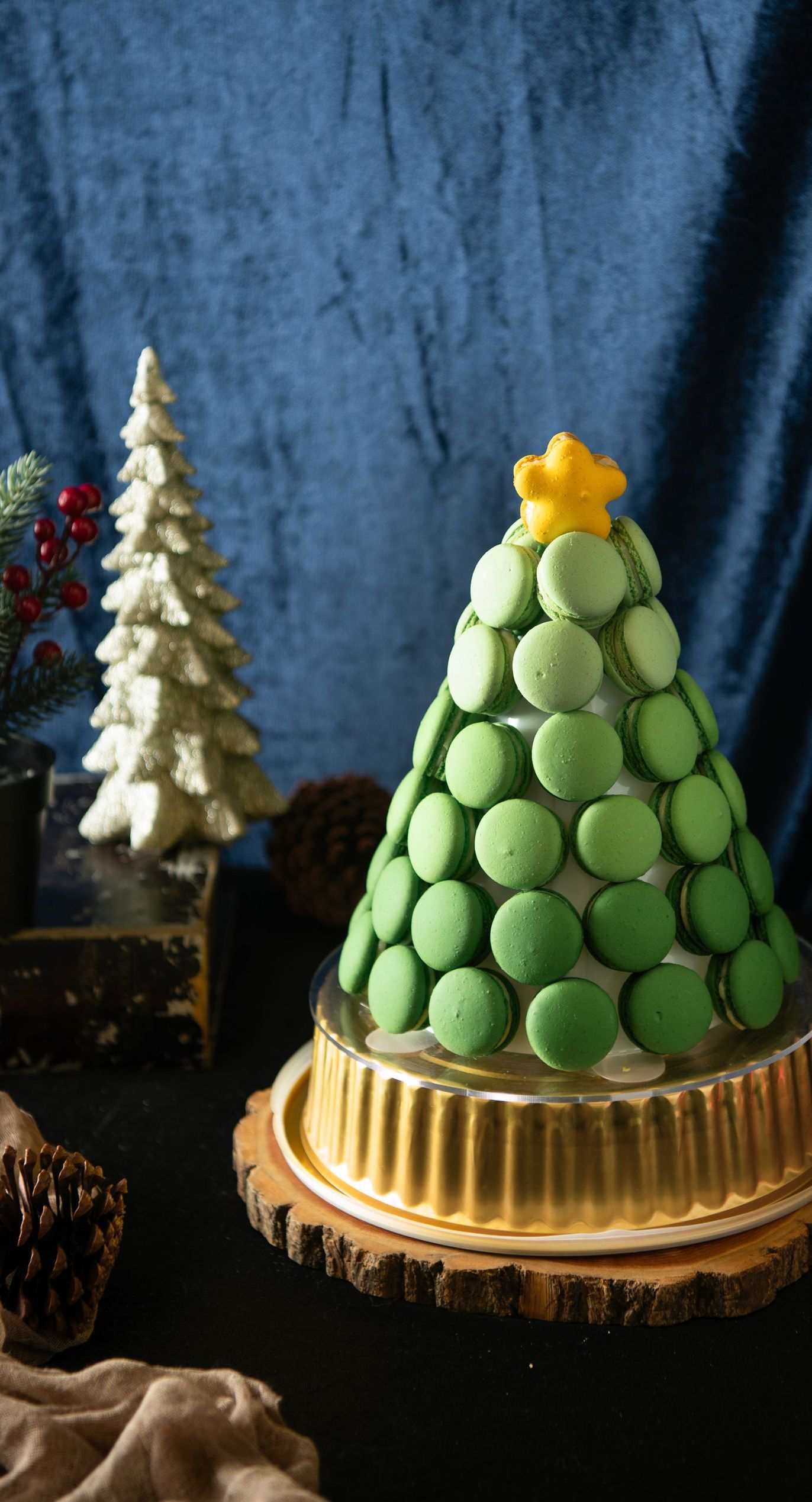 Green macaron Christmas tree on a cake stand, decorated with a yellow star on a blue backdrop.