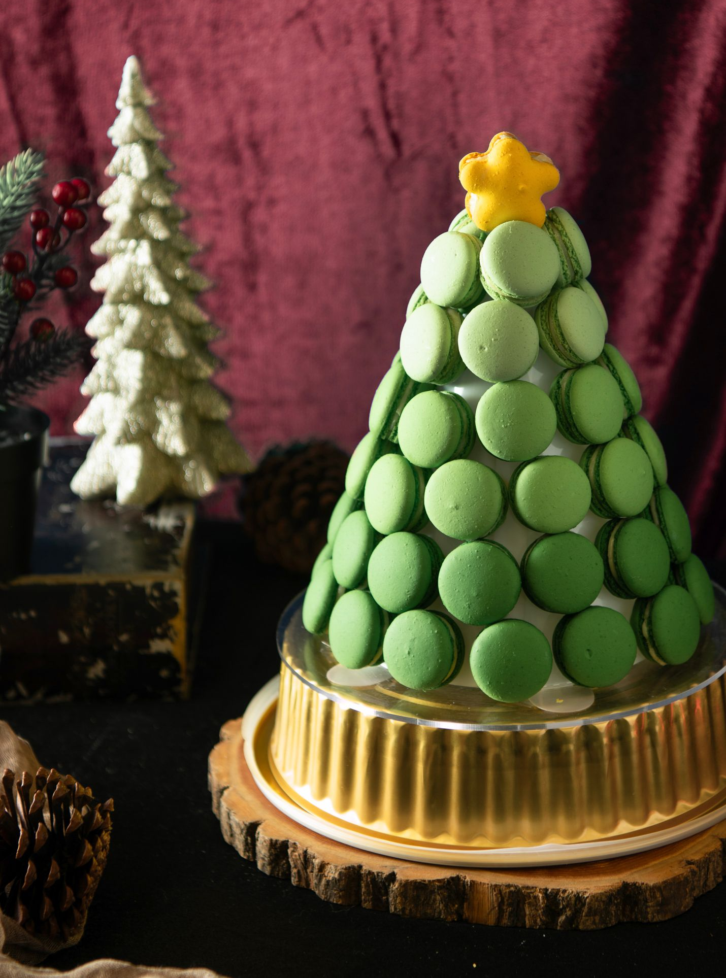 Green macaron Christmas tree on a golden base, topped with a yellow star, against a burgundy backdrop.