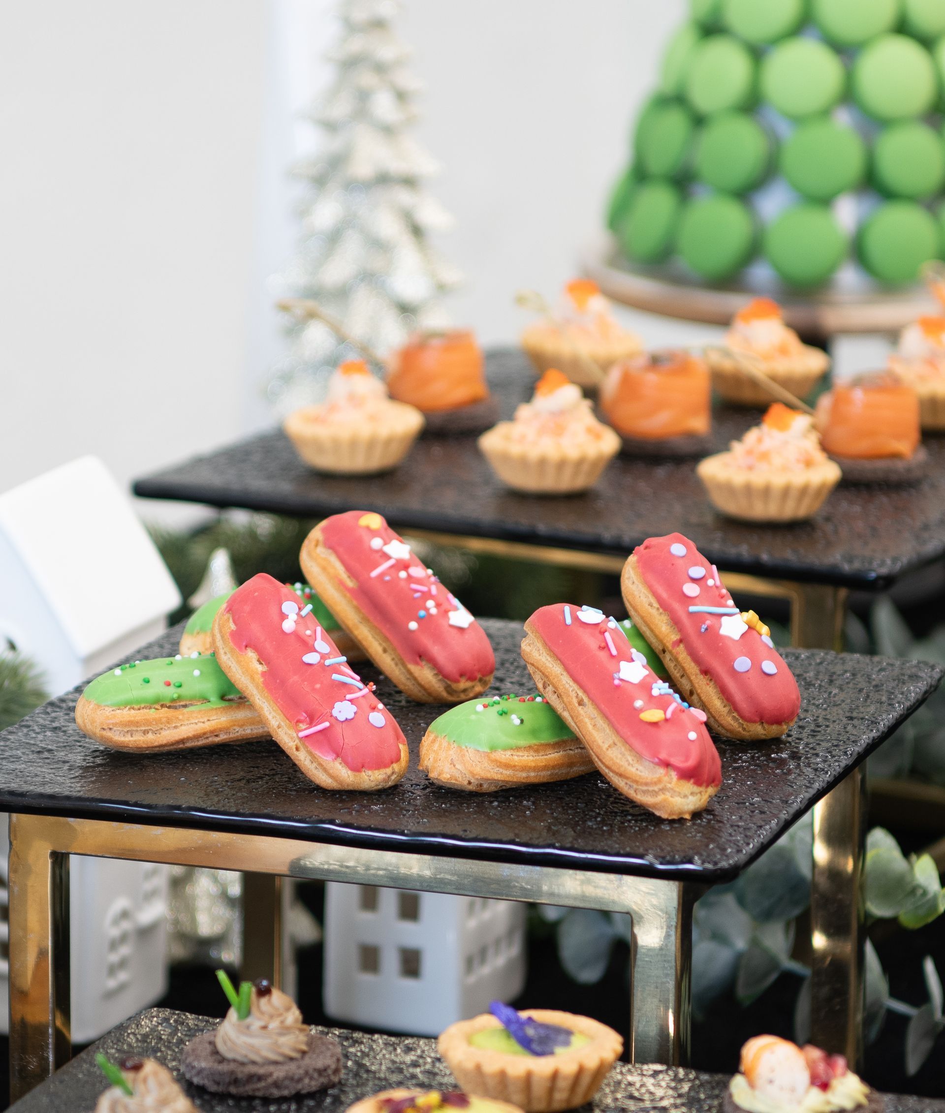 Dessert display: eclairs with red and green icing, mini tarts, and orange appetizers.