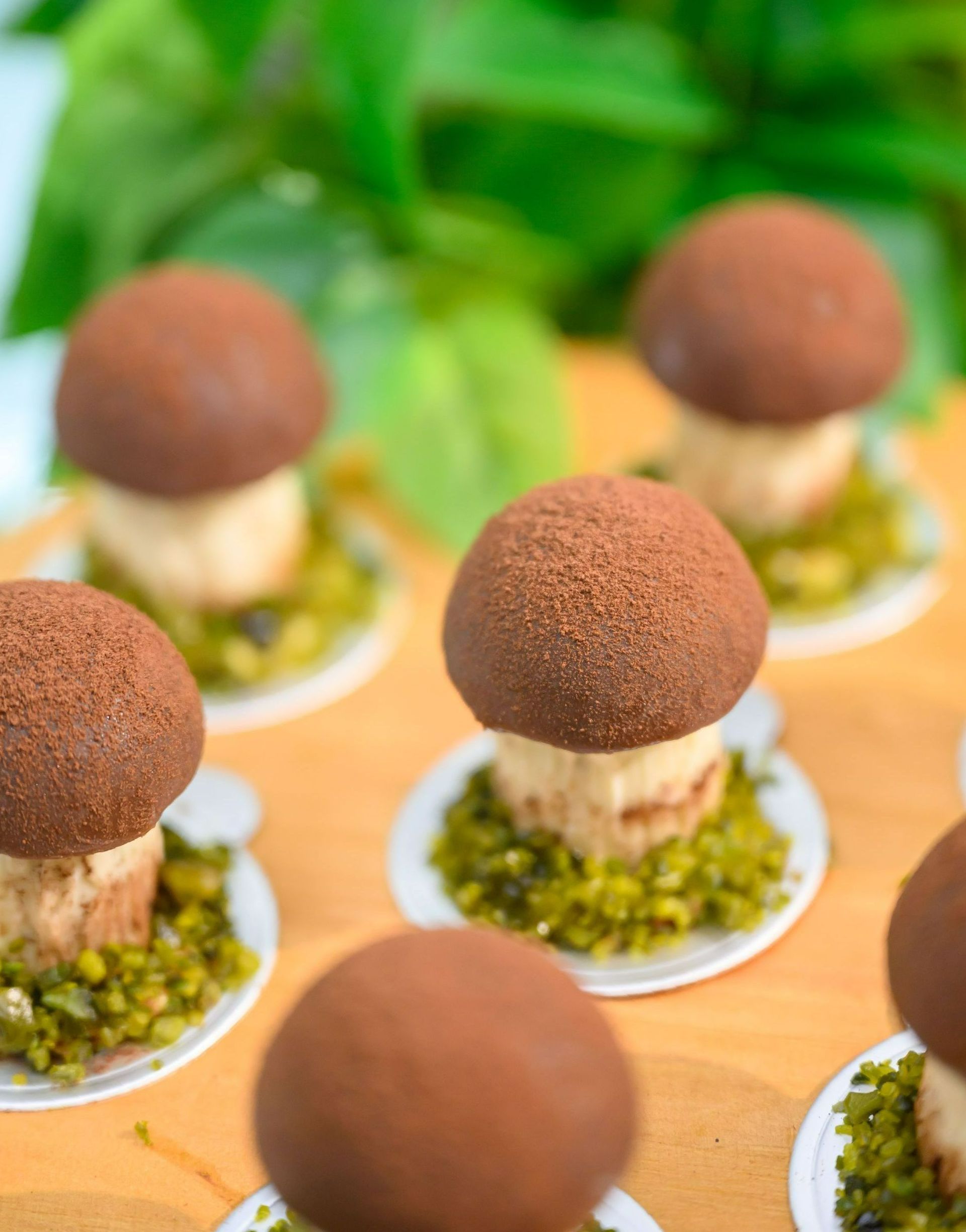 Mini mushroom-shaped desserts on small plates, set on a wooden surface with green garnish.