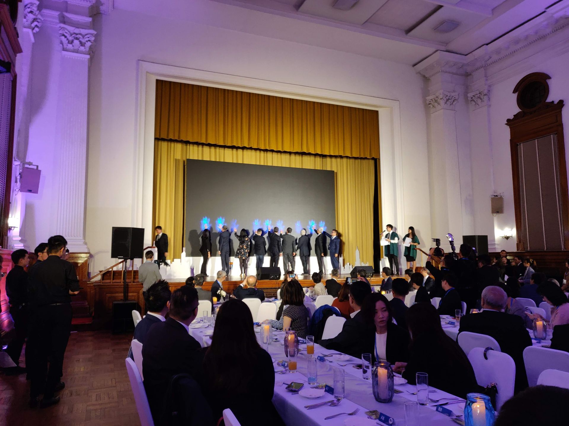 People watching a performance on stage at a formal event, with tables and chairs.