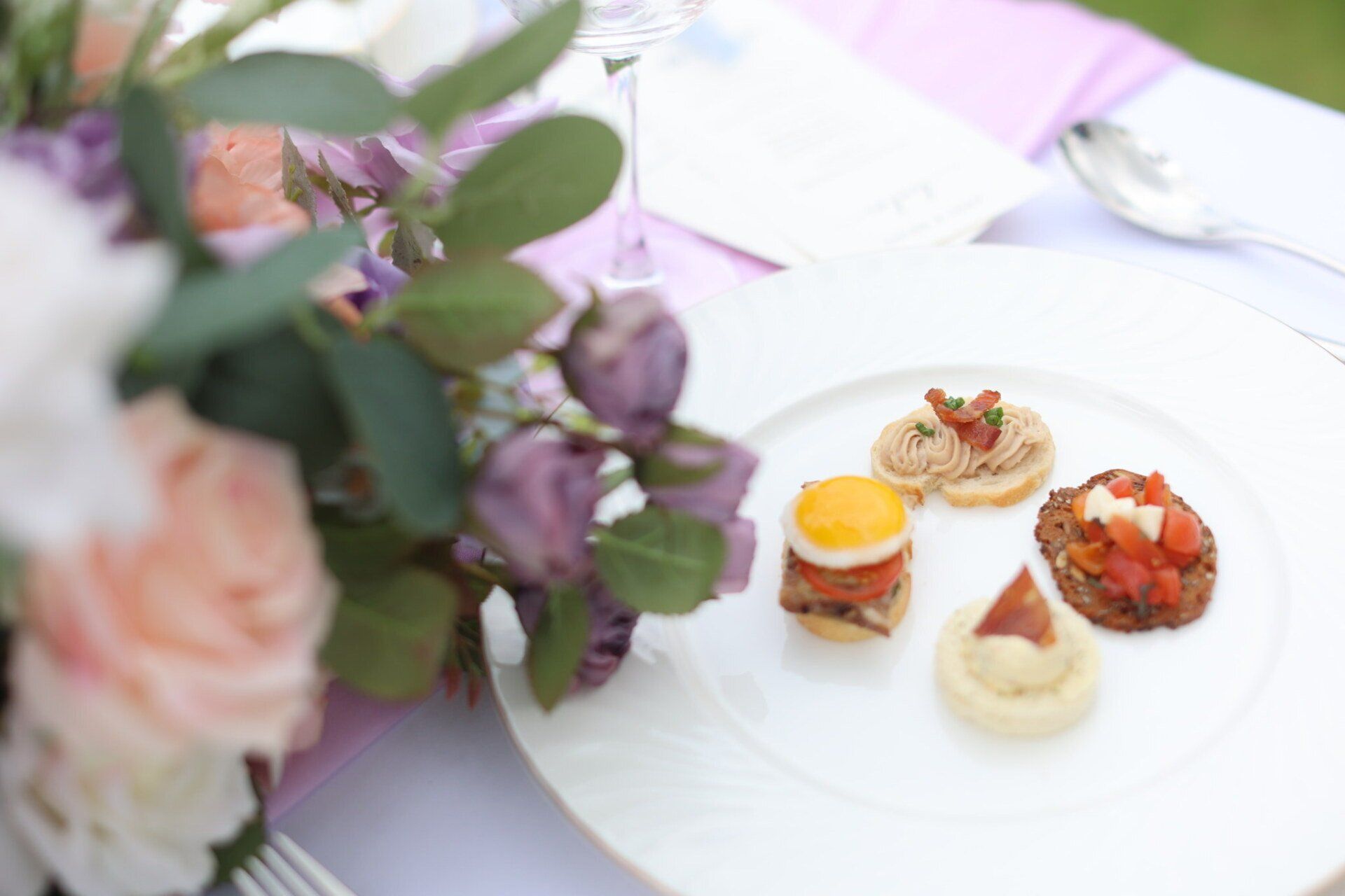 White plate with appetizers, next to flowers and silverware on a table.