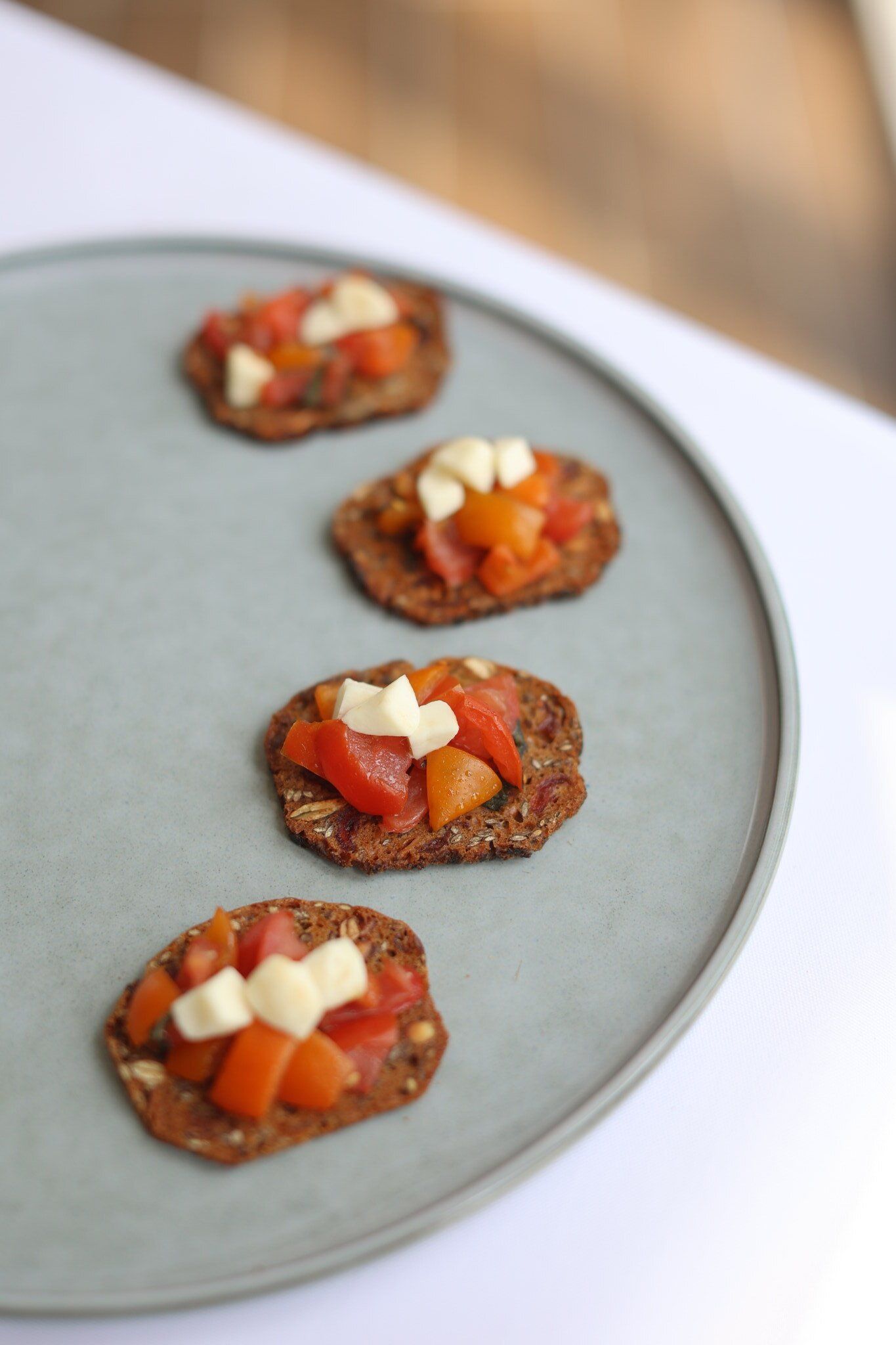 Appetizers on a blue plate: crackers topped with tomatoes and cheese.