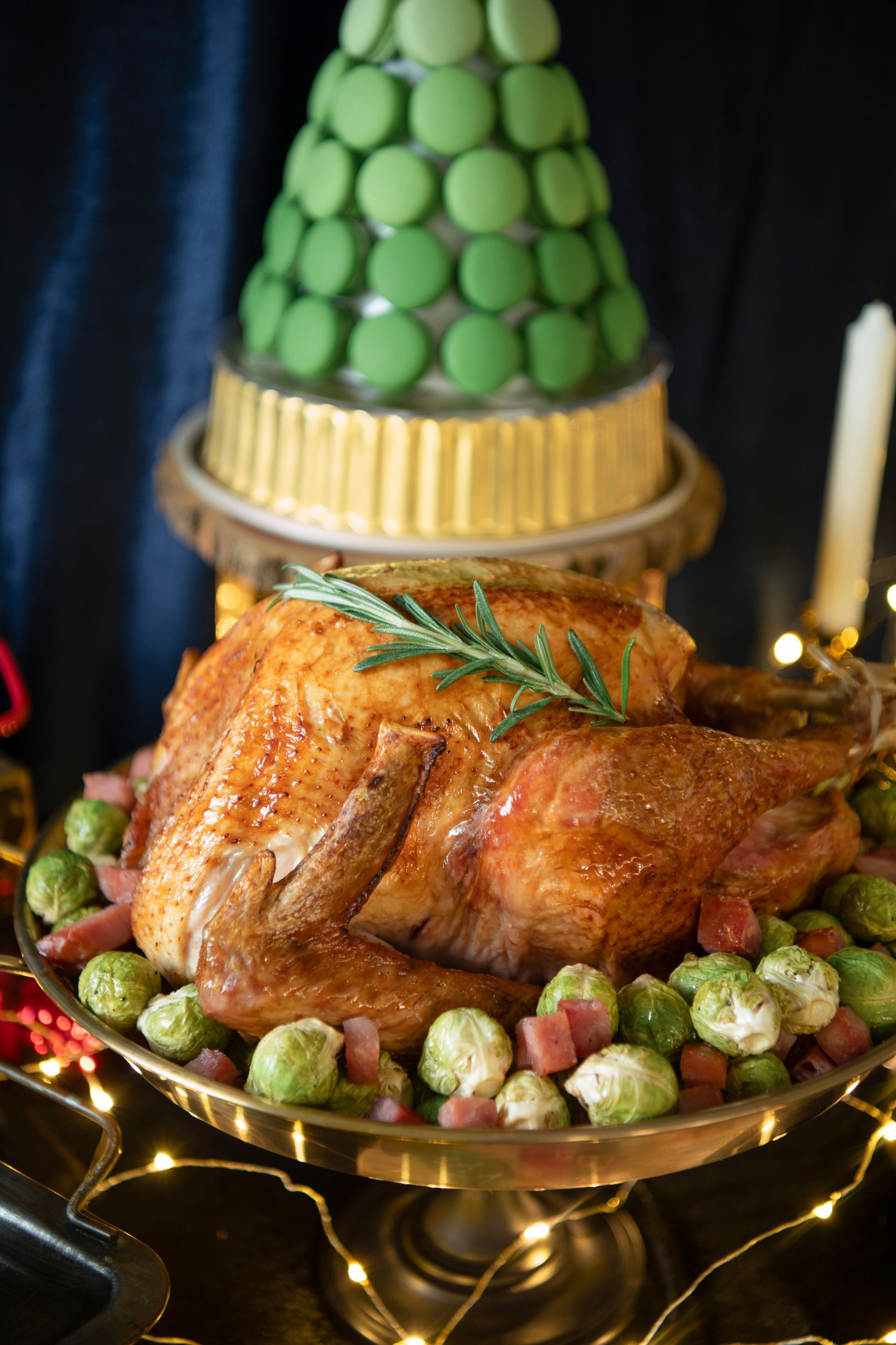 Roasted turkey on a platter with Brussels sprouts, decorated for a holiday feast, with macaron tree in background.
