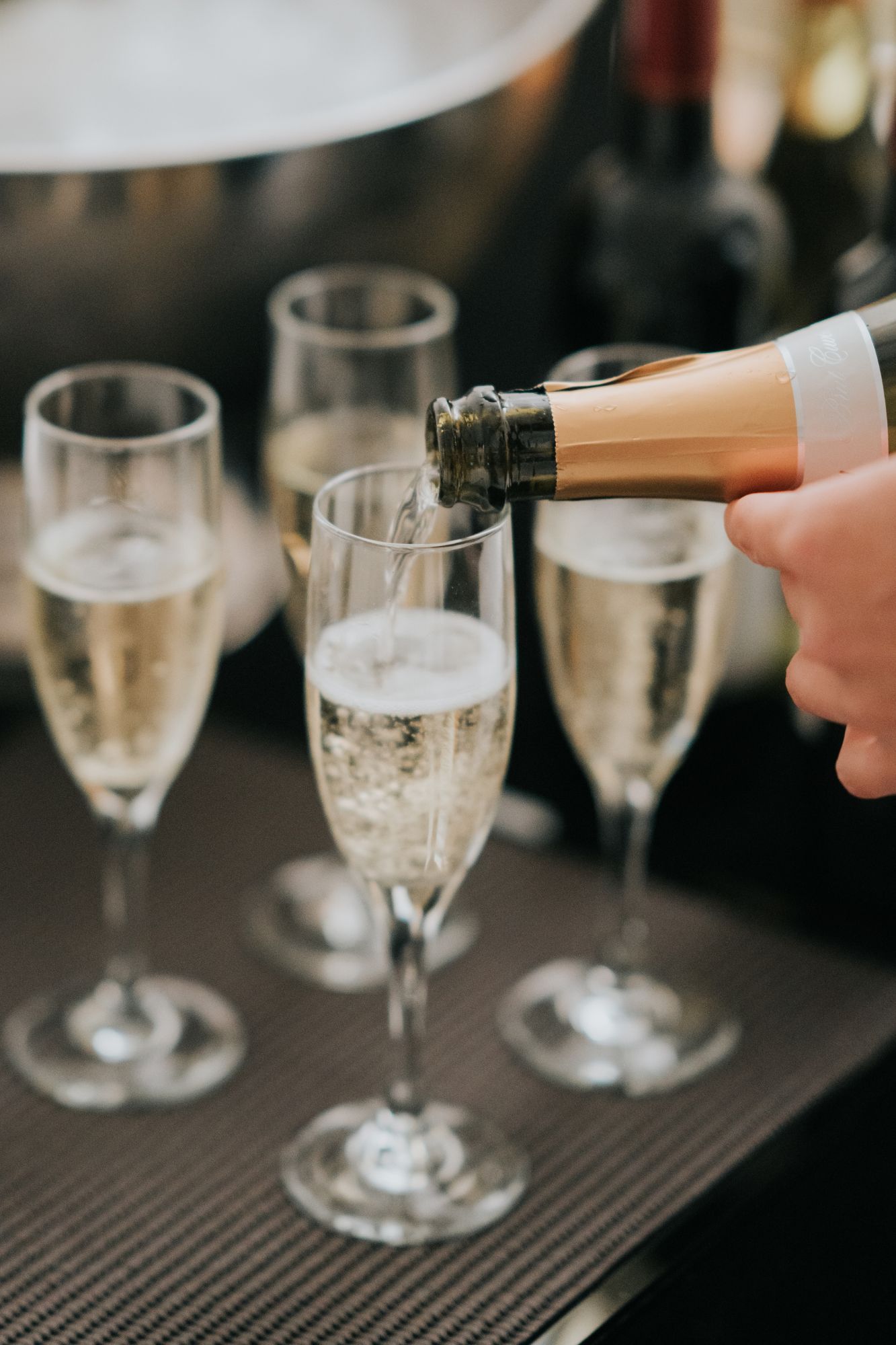 Champagne being poured into a flute glass, with three filled glasses on a tray.