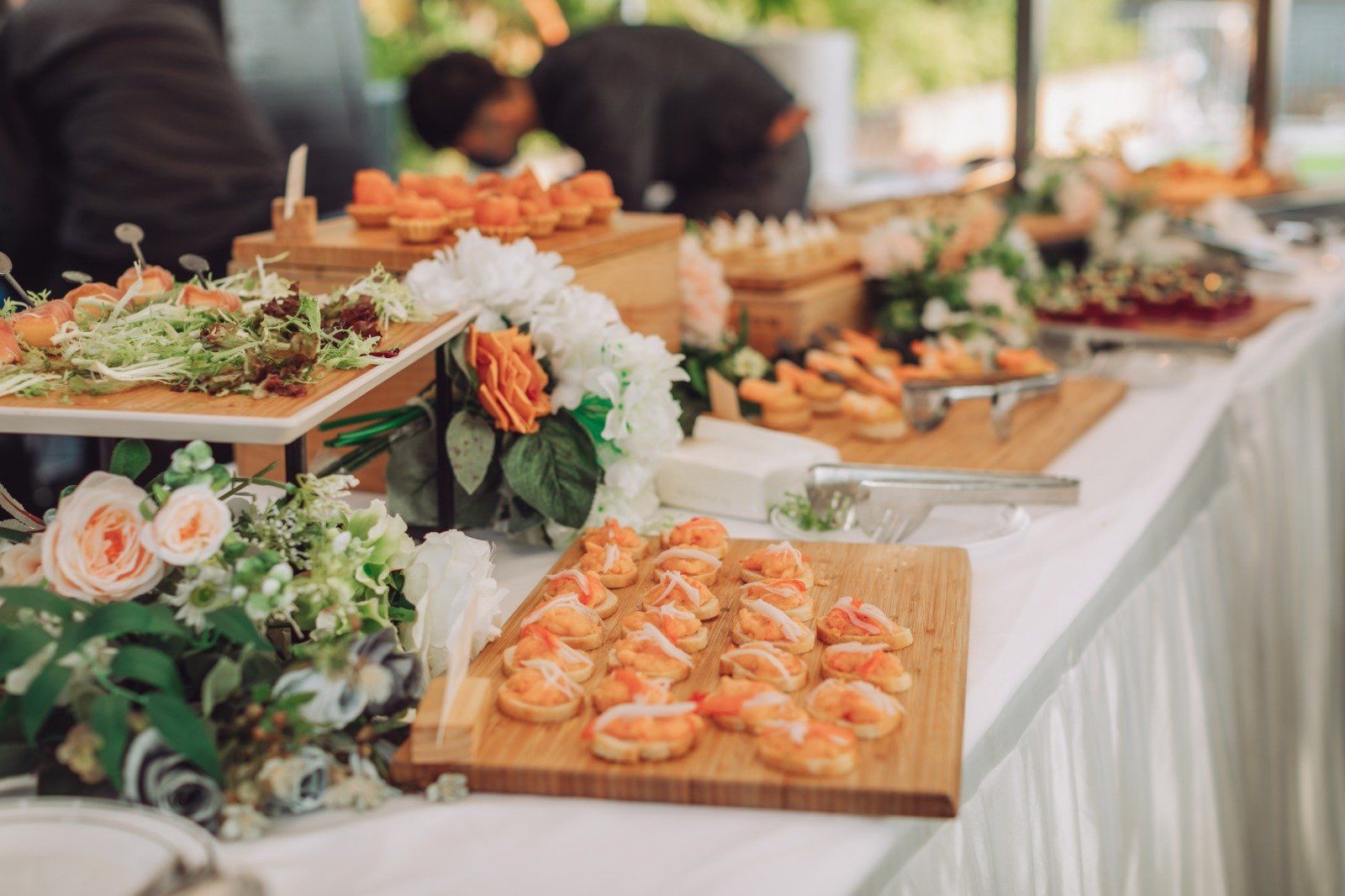 Buffet table with various appetizers, flowers, and a person in the background.