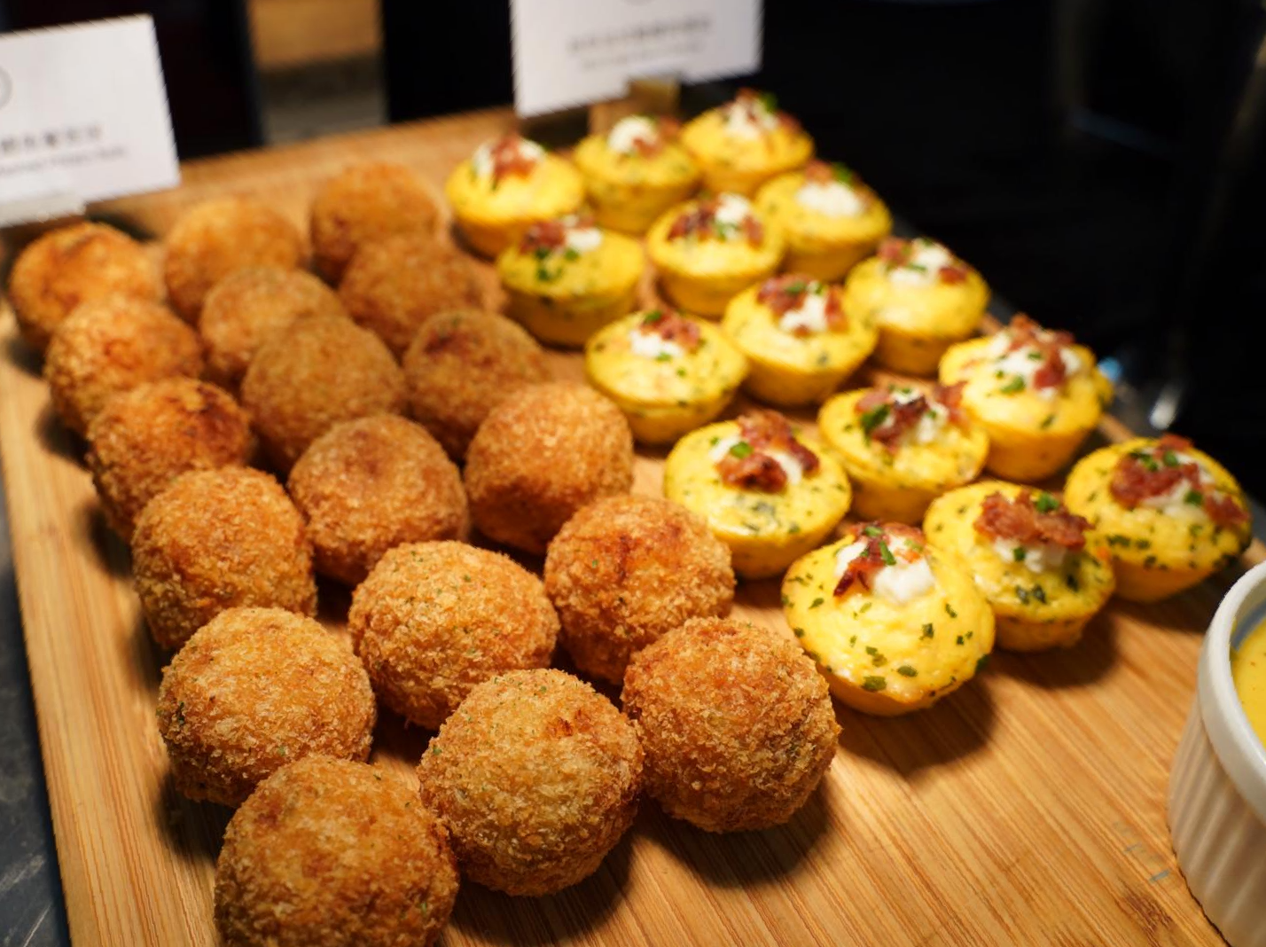 Tray of appetizers: breaded balls and mini quiches with toppings, on a wooden board.
