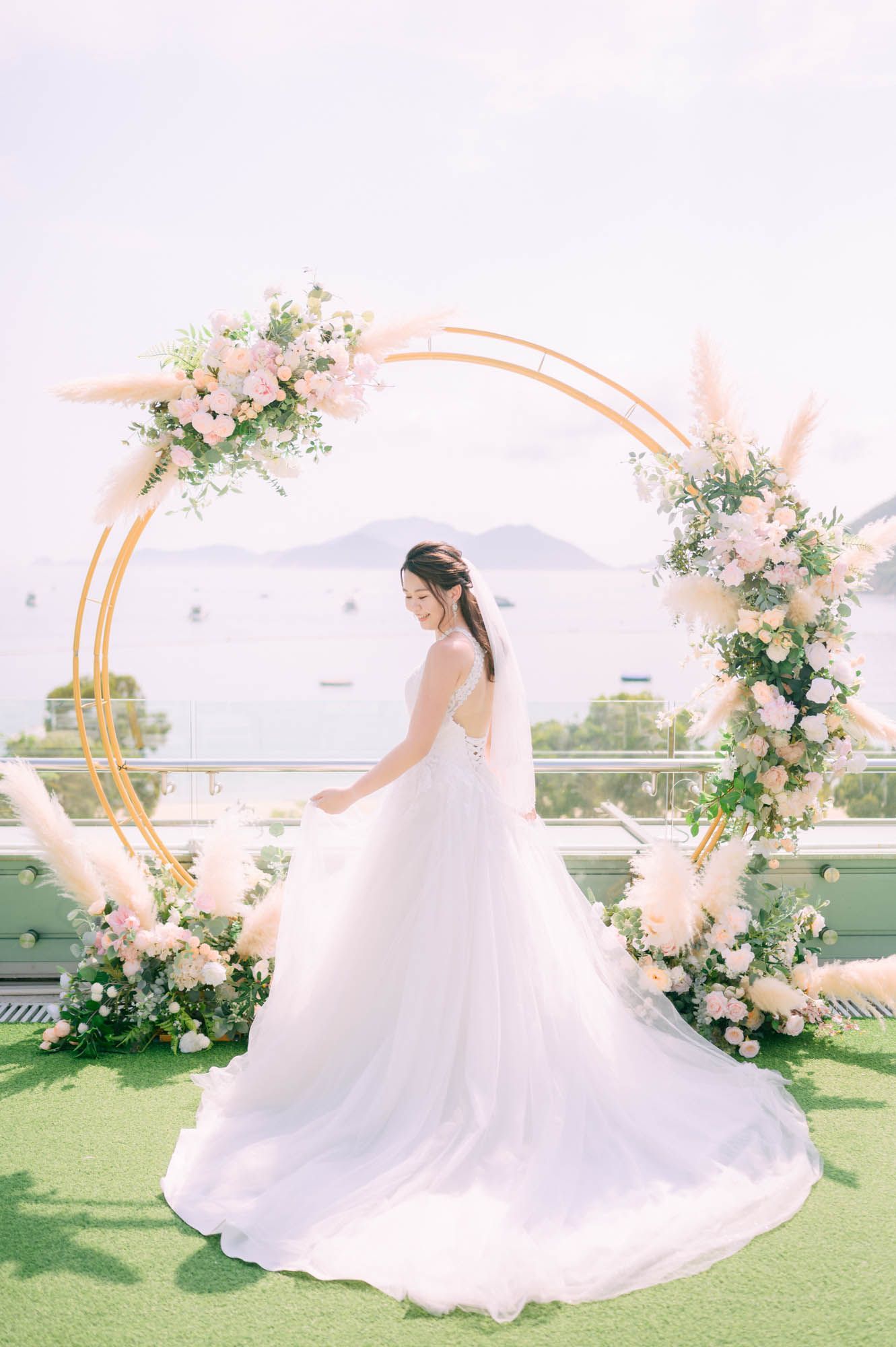 Bride in white gown twirls near a gold floral arch with an ocean view.
