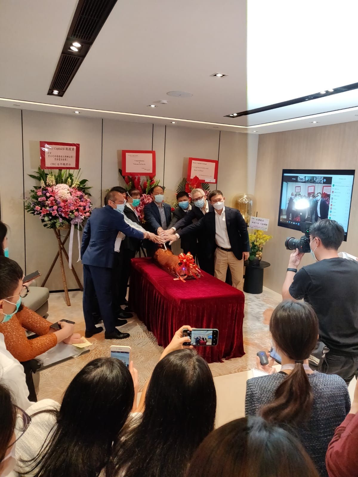 People gathered around a red-covered table, hands clasped together, possibly for an opening or celebration event.