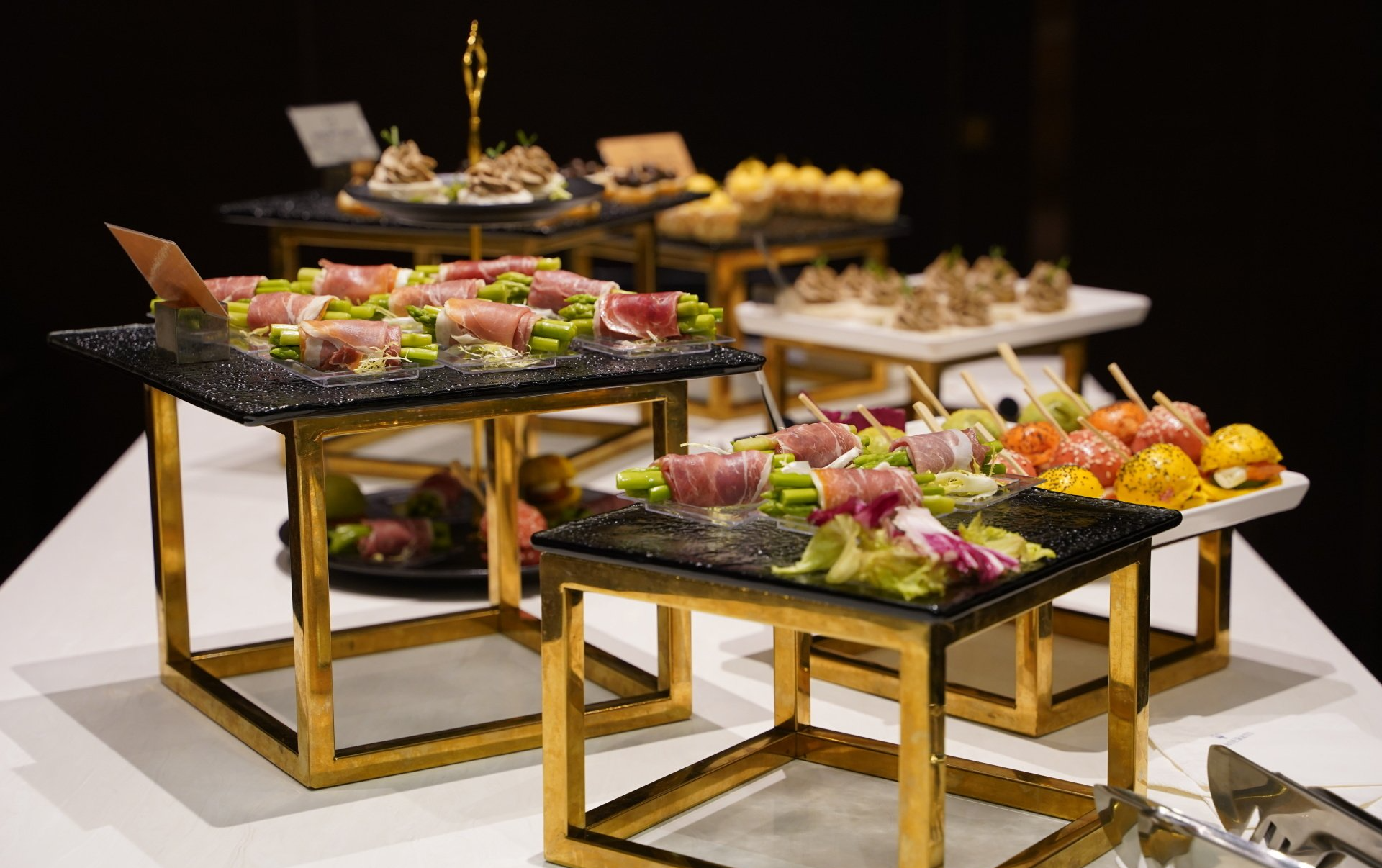 Buffet table with appetizers on tiered trays; gold frames, black surfaces.