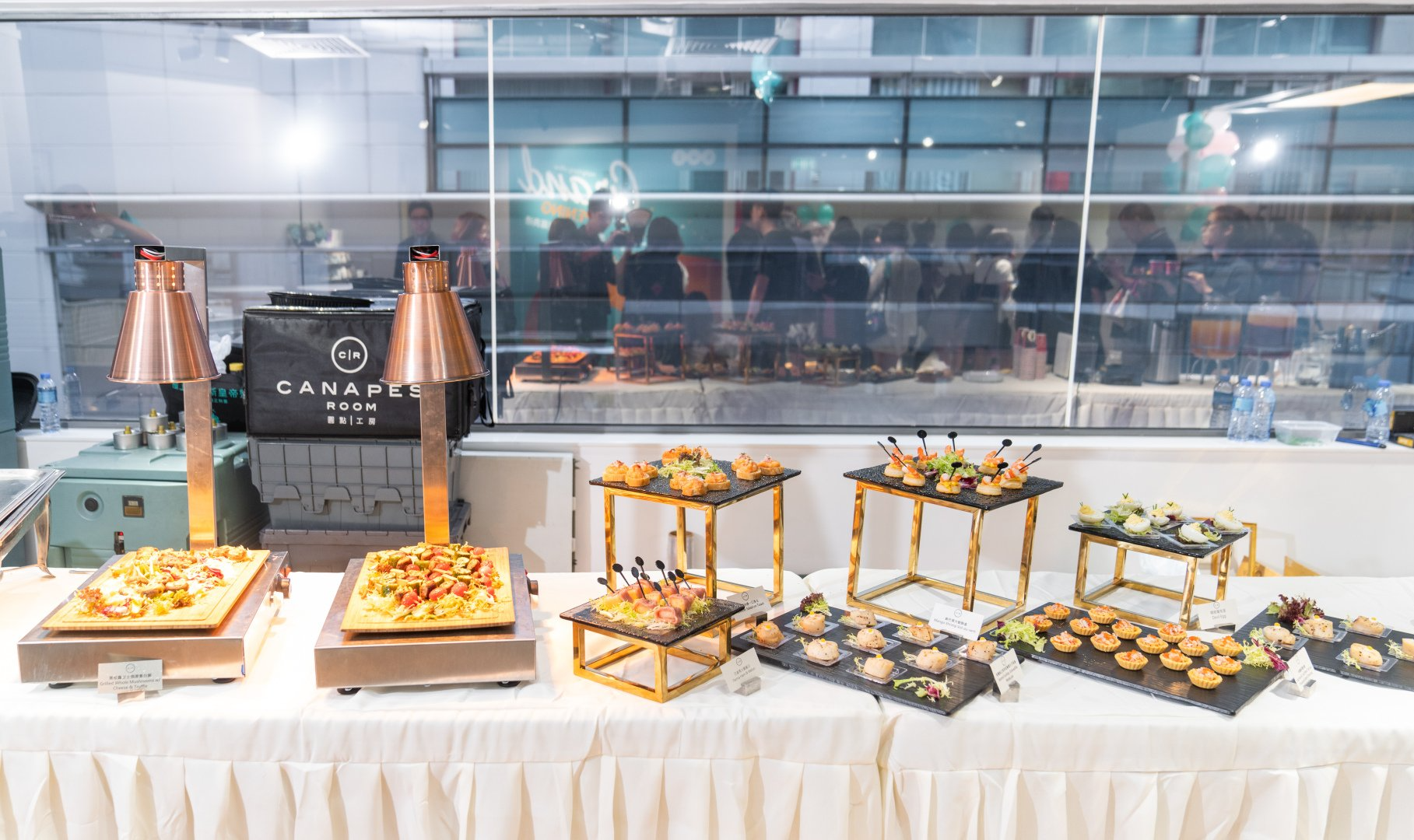 Buffet with various food platters, warming lamps, on white tablecloth, indoors.