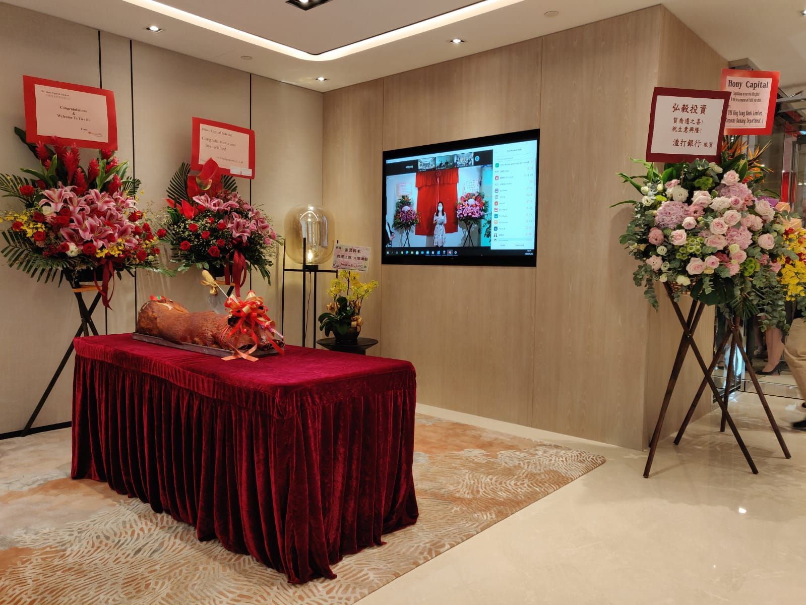 Room with a red table, flowers, and a screen displaying a ceremony.