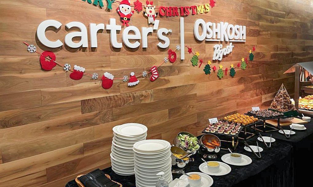 Carter's | Oshkosh B'gosh 聖誕自助餐。木牆上裝飾著聖誕飾品，擺放著食物和堆疊的餐盤。