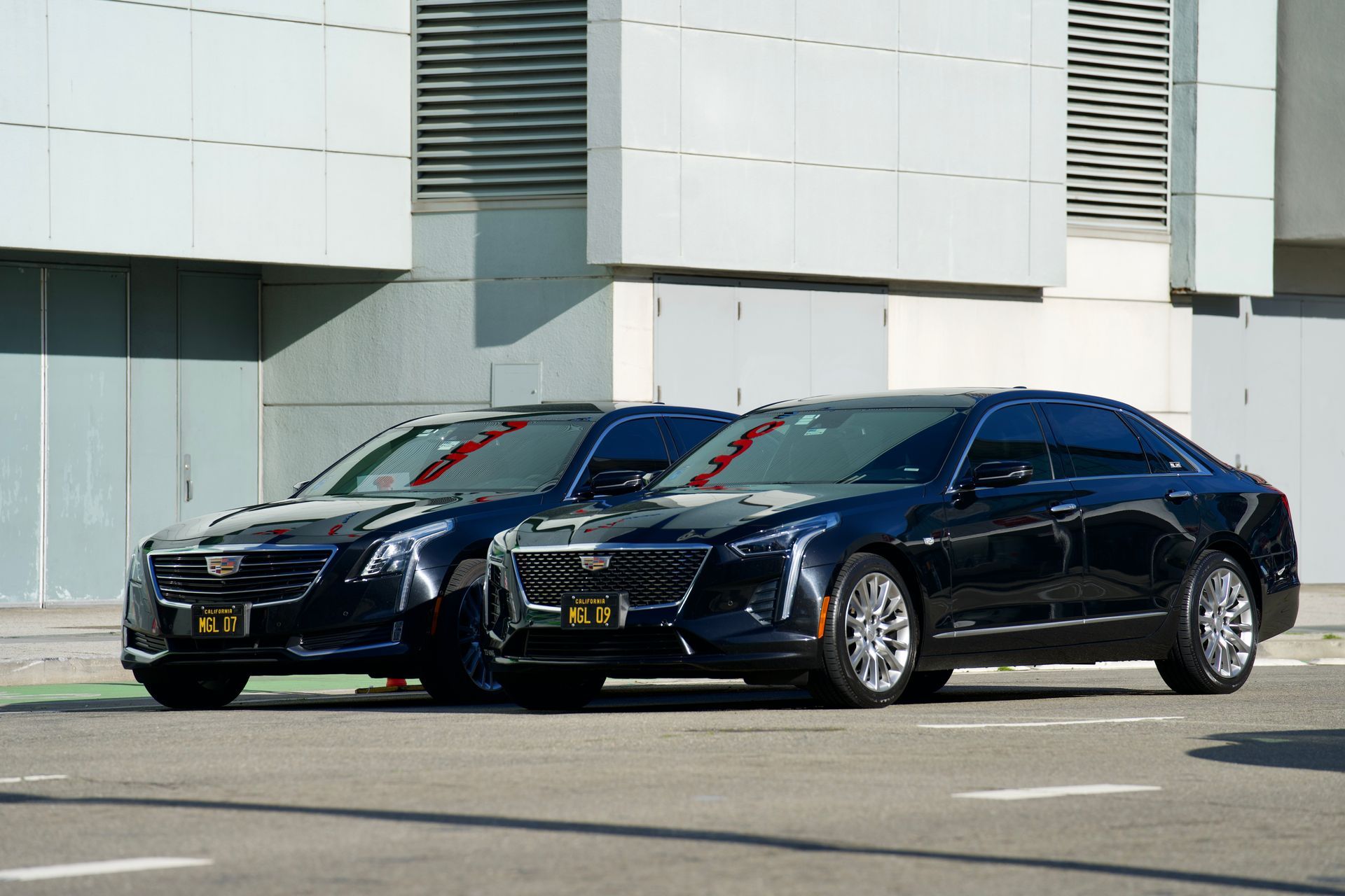 Two black sedans parked in front of a building on a sunny day.