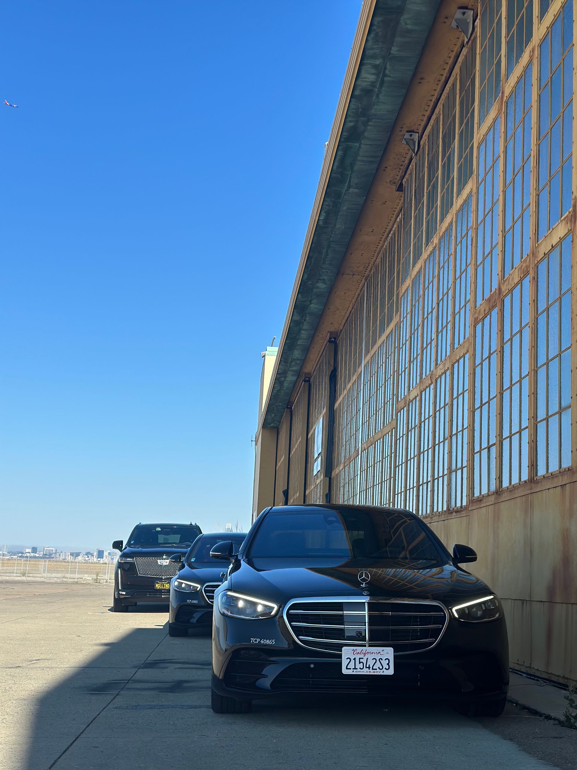 Three black luxury cars parked next to a large building with windows; clear blue sky overhead.