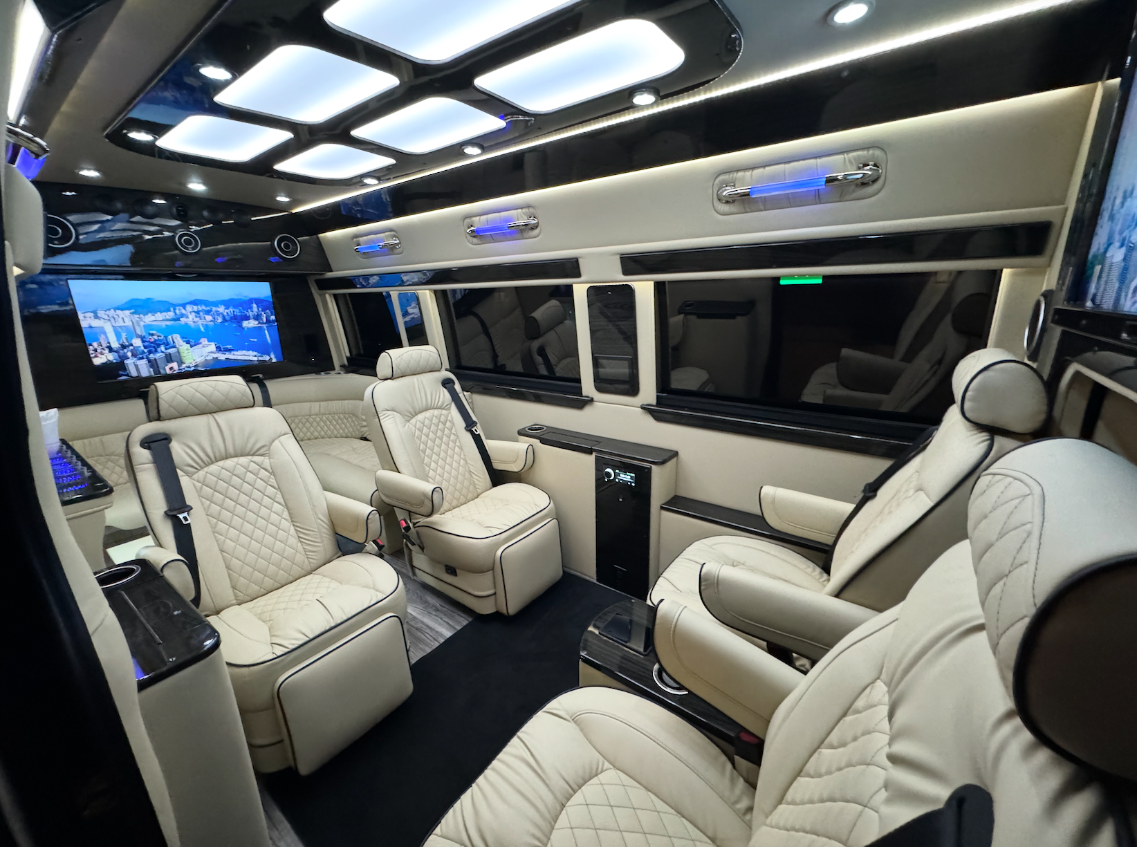 Luxurious van interior with cream leather seats, multiple screens, and ambient lighting.