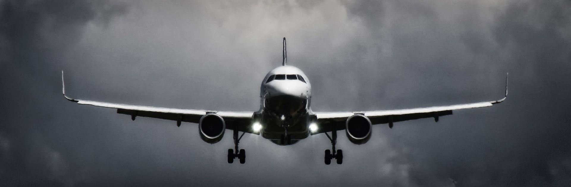 Airplane approaching head-on with landing gear down in a dark, cloudy sky