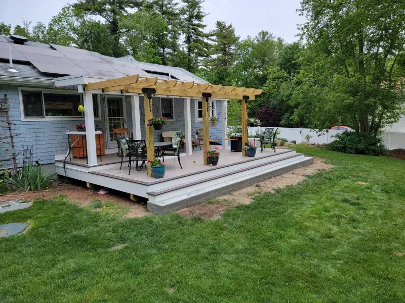 Wooden deck with pergola, seating area, and potted plants, in a backyard setting with green grass.