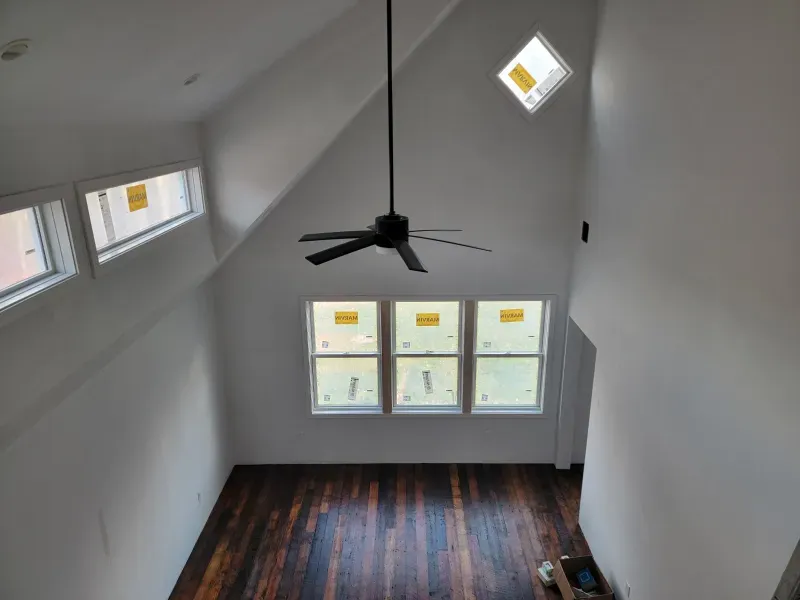 Interior view of a room with angled ceilings, multiple windows, and a ceiling fan. Dark wood floor.