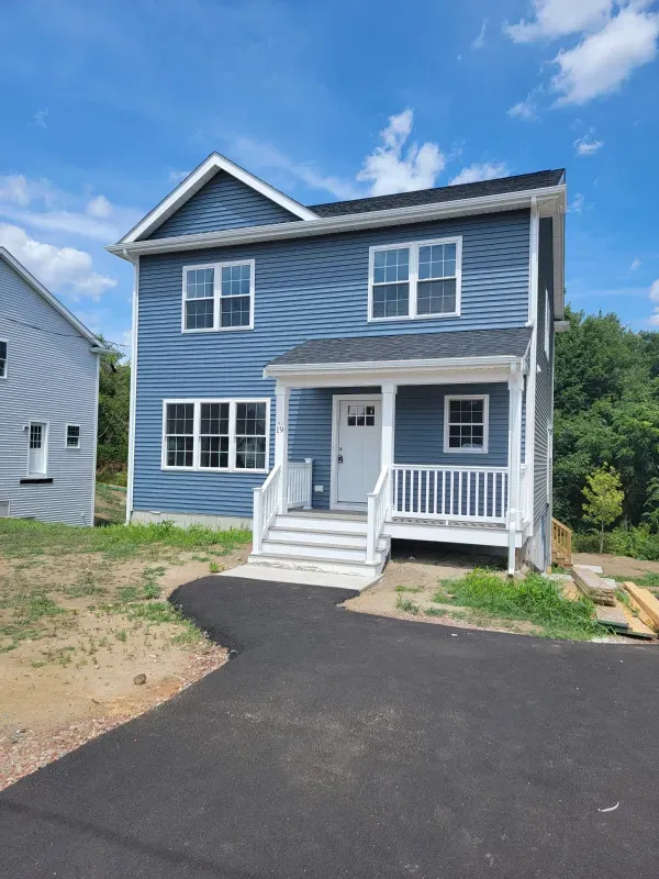 Blue two-story house with white trim, front porch, and black driveway under a blue sky.