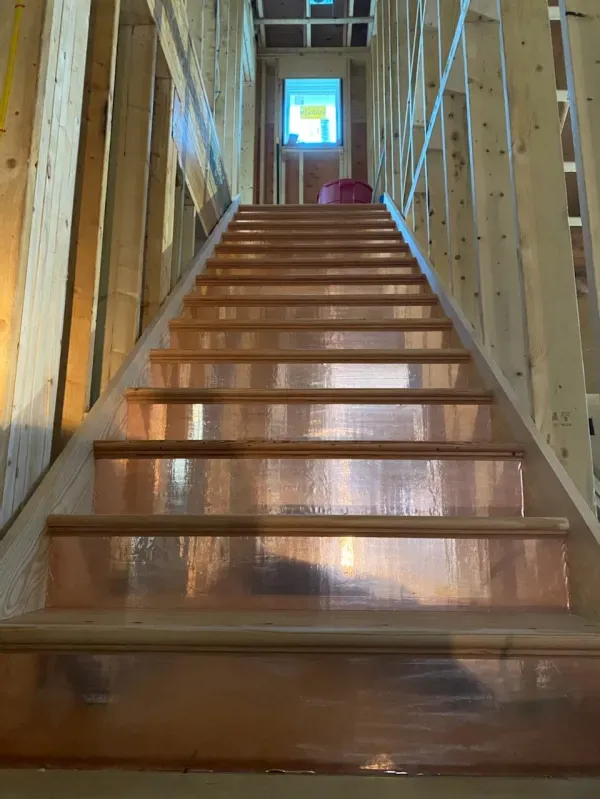 Wooden staircase with copper treads, leading upwards toward a window, under construction.