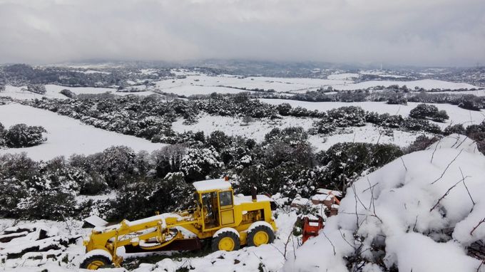Spazzaneve giallo che libera una strada innevata, con vista su una valle invernale