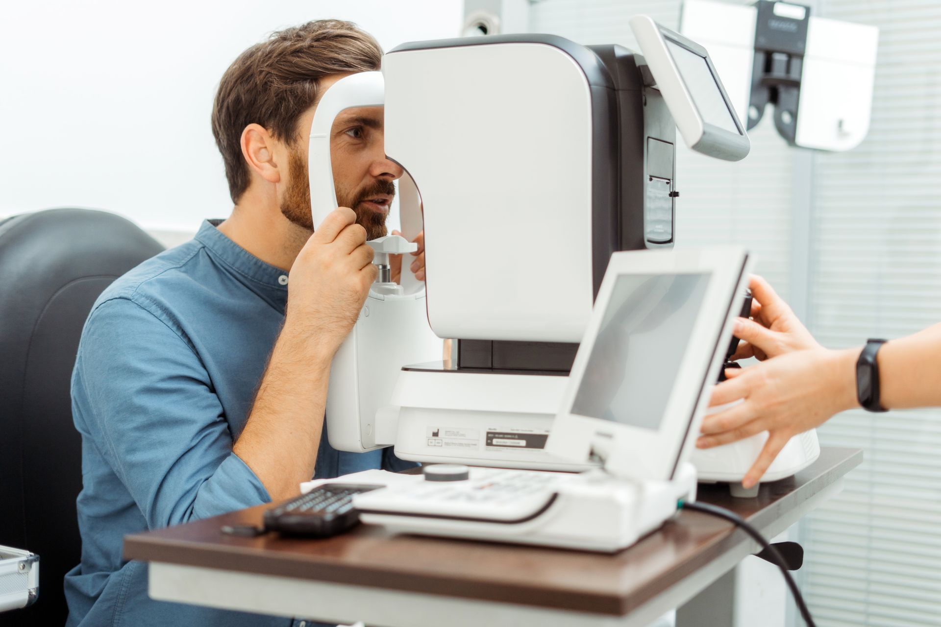 Person using an eye exam machine in an optometrist’s office with a technician beside it