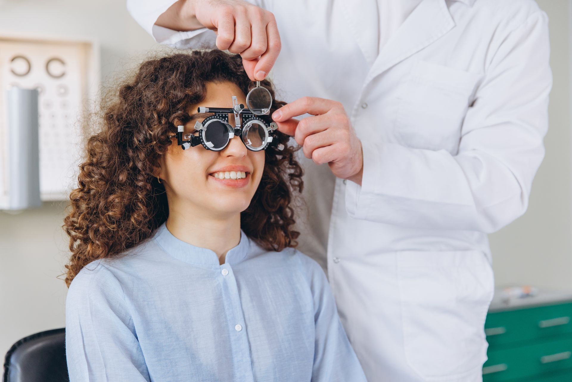 Optometrist adjusting phoropter on smiling patient in an eye exam room