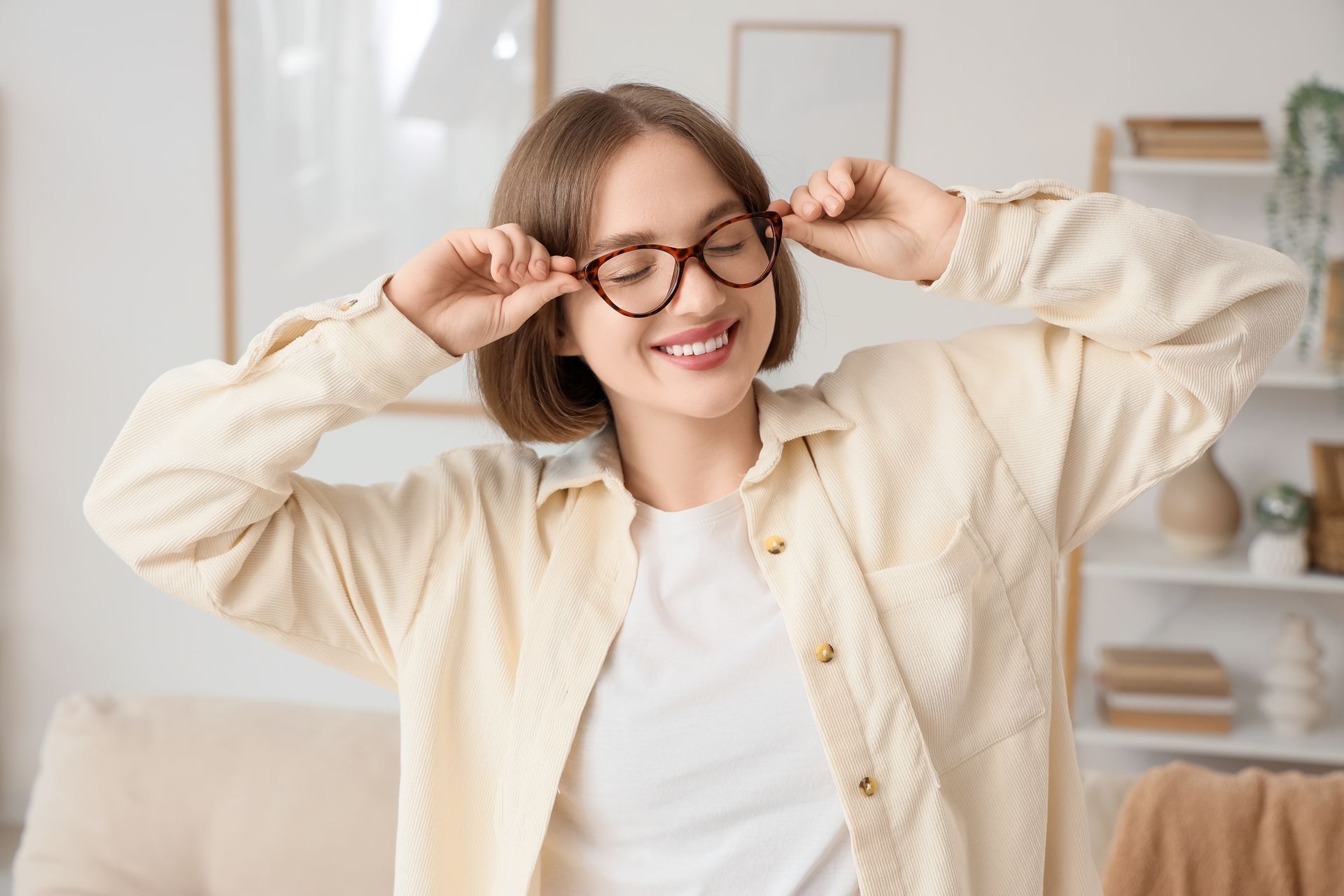 Smiling woman adjusting glasses in a bright, cozy room