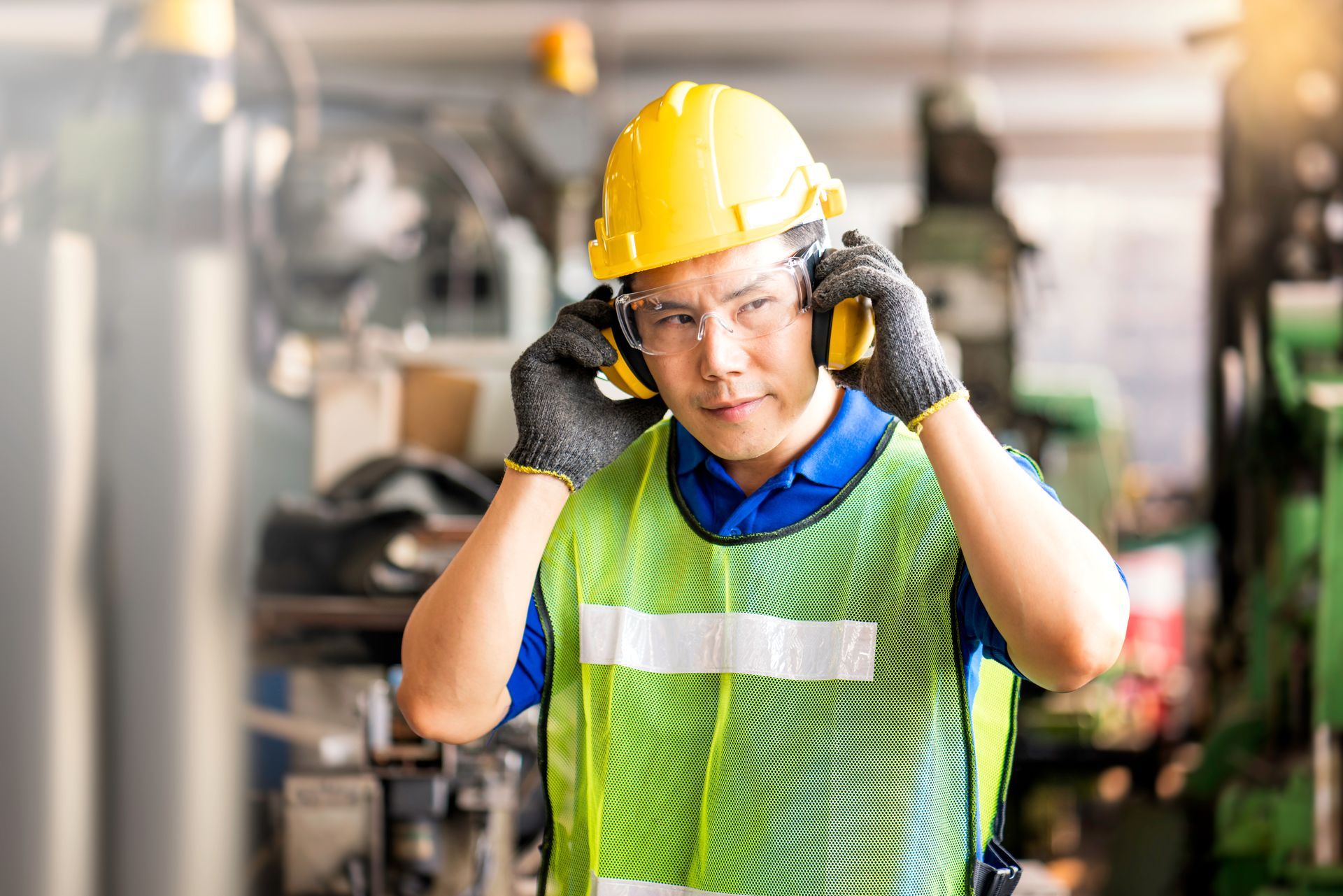 Worker in yellow hard hat adjusting gloves in an industrial factory setting
